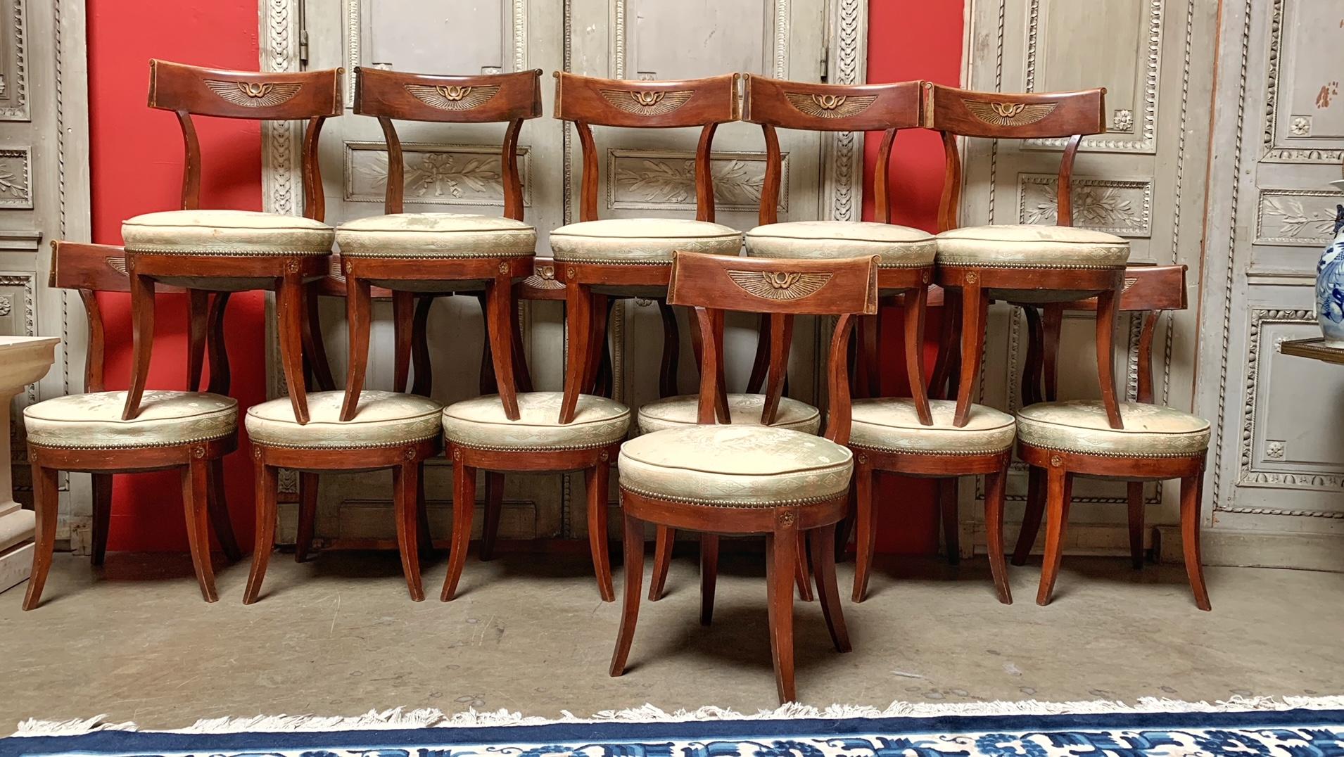 Twelve Regence style dining chairs with klismos style legs and a double headed eagled carved on each chair. They are not large chairs but are comfortable. The few of the chairs have had some old repairs and could be refinished or lacquered. They