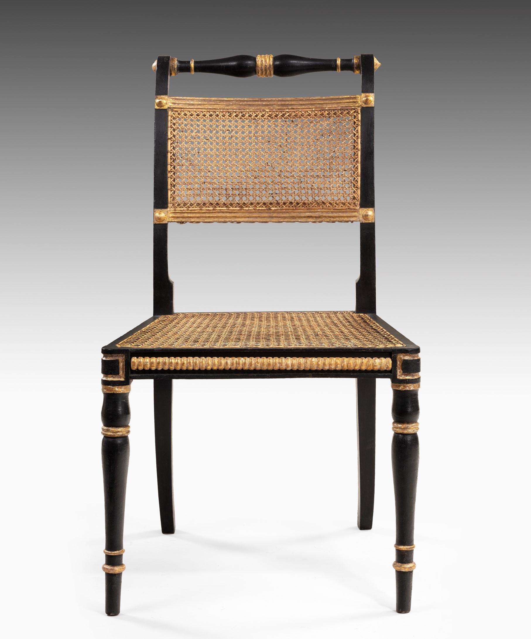 An elegant set of twelve Regency dining chairs with original ebonized and gilt decoration; the dining chair's ring turned top rail above a caned back and a caned seat with the seat rail decorated with gilded coin moldings. The dining chair is raised