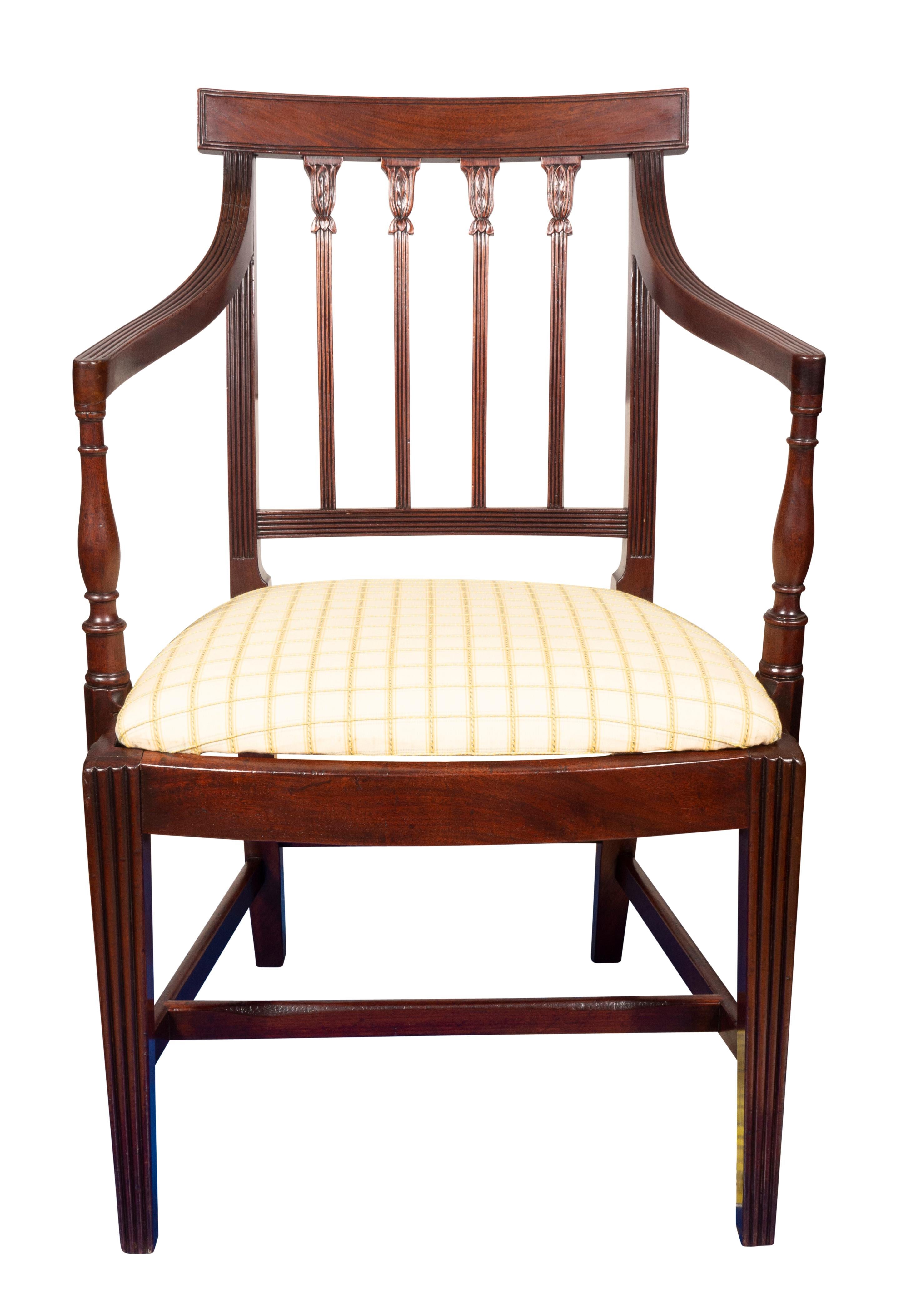 Comprising ten side chairs and two armchairs. Each with a rectangular shaped crest rail over a reeded and leaf carved spindle back , bowed seat frame, drop in seats raised on reeded square tapered legs joined by an H form stretcher. Provenance: N.P