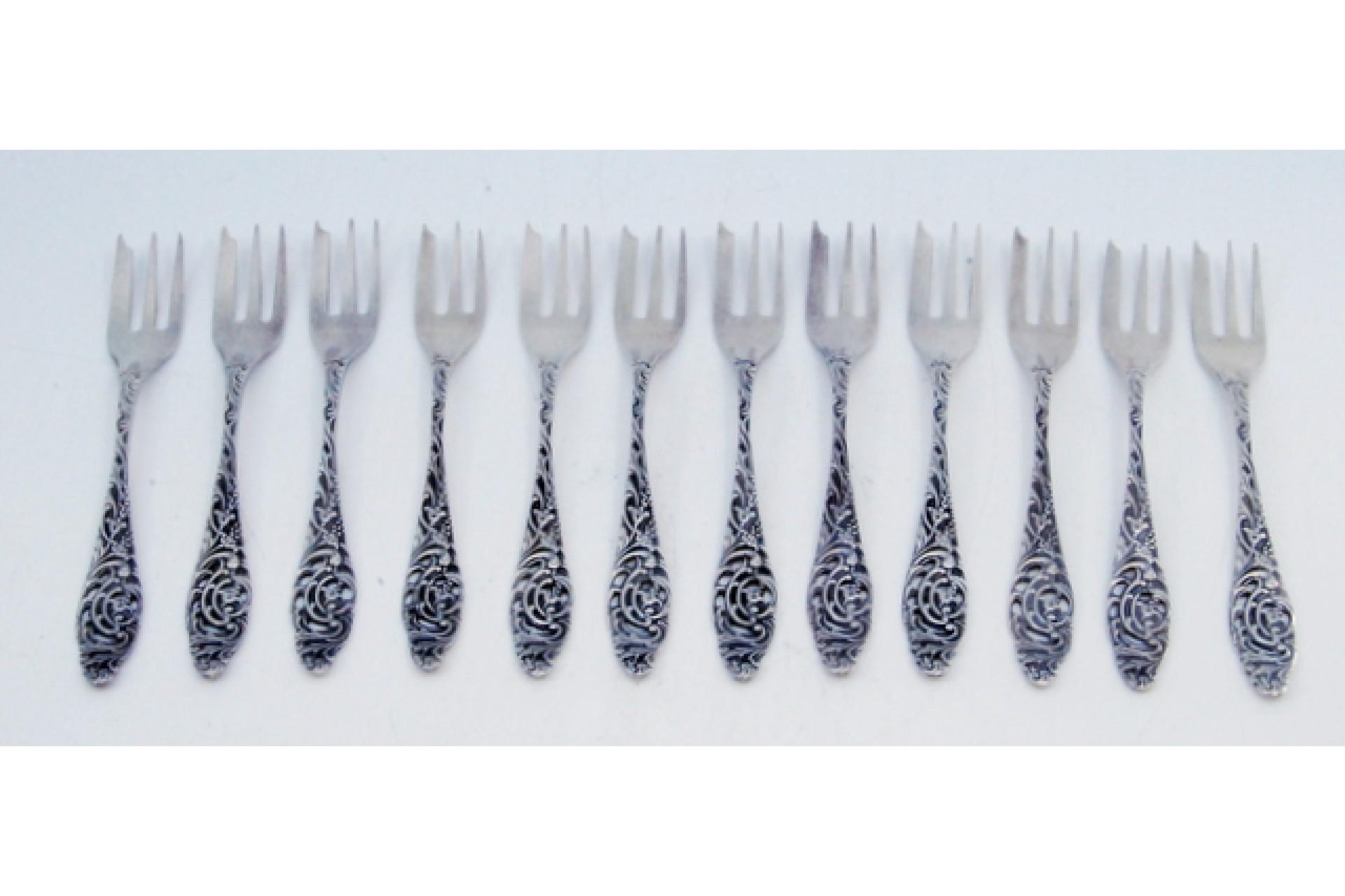 Description: Set of twelve silver cake forks with embossed handles featuring plant motifs. Metal: Silver. Origin: European. Brand: Unknown. Weight: 148.74 grams (Set of twelve forks). Dimensions: 12.2x1.6cm. Content: 900/1000. Assay Mark: Yes.
