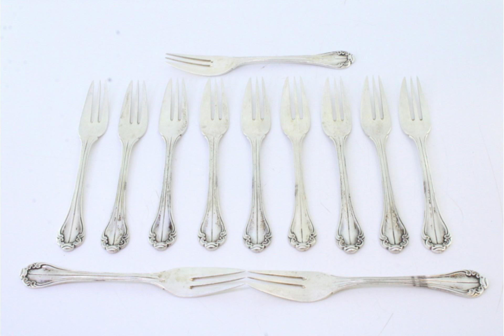 Description: Set of twelve silver cake forks with grooves and shells along the handles. Metal: Silver. Origin: Portuguese. Brand: Cabeça de escravo. Weight: 312.46 grams (Set of twelve forks). Dimensions: 2cmx13.5cm. Content: 916/1000. Assay Mark: