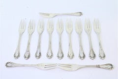 Set of twelve silver cake forks with trim and shells along the handles