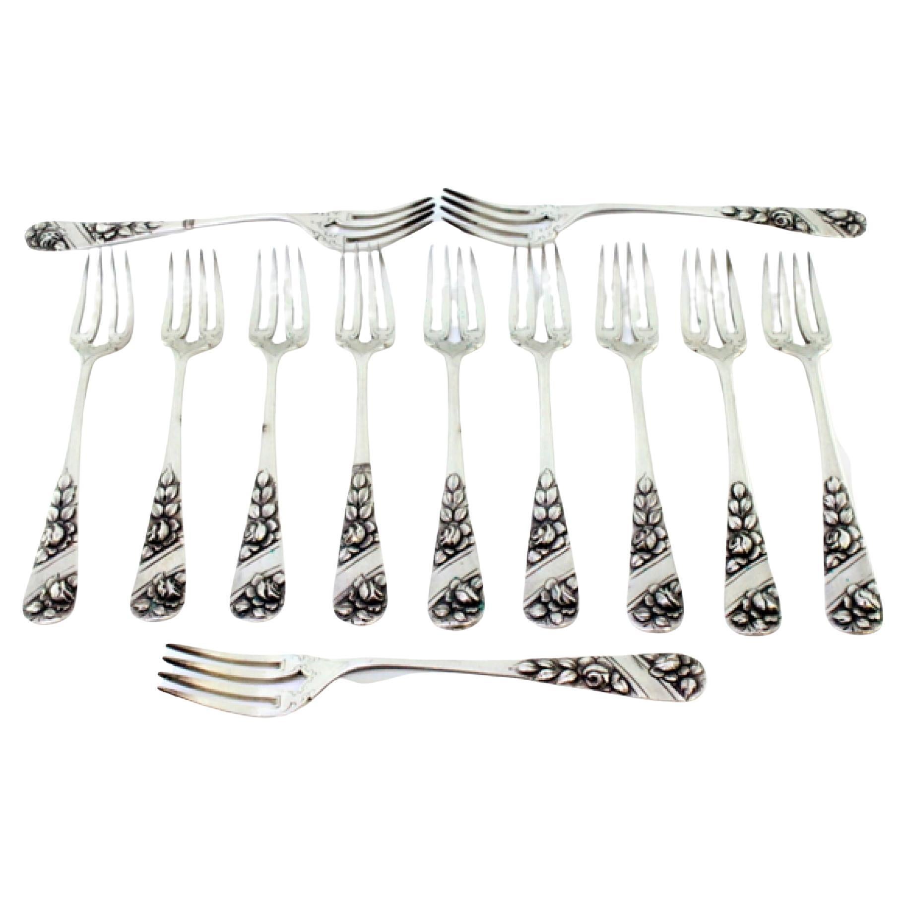 Set of twelve silver forks w/ reliefs on the handles surrounding monogram cards