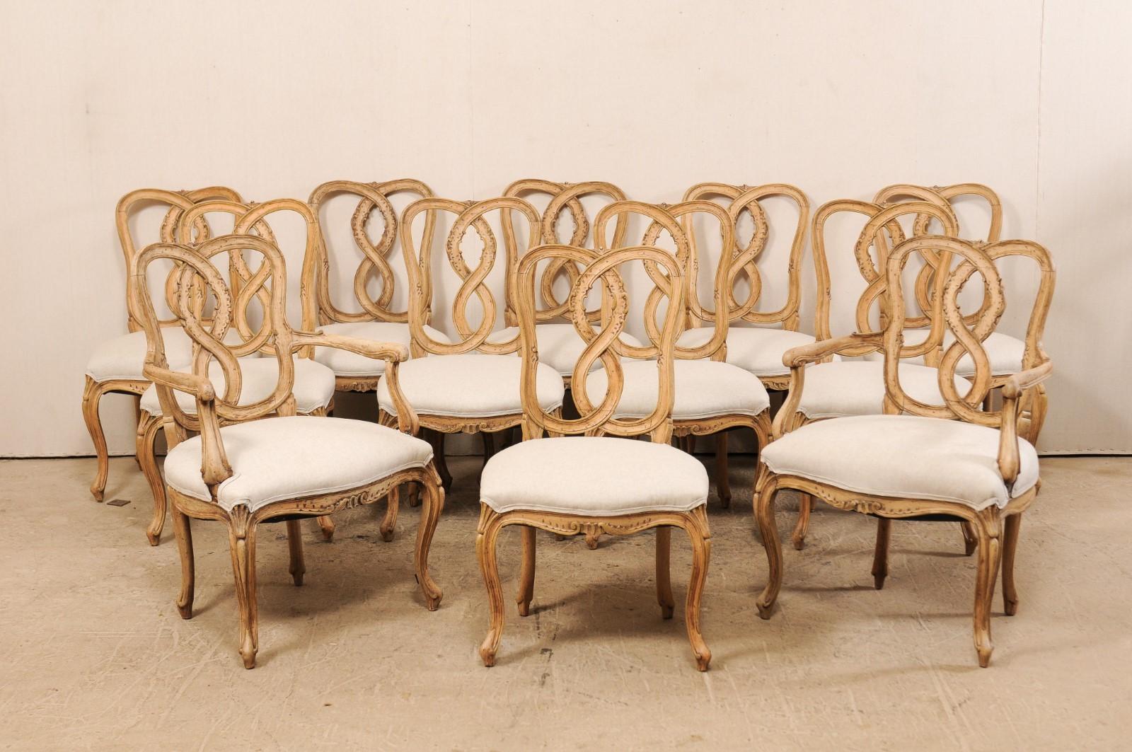 Set of twelve American made, Italian Venetian style carved wood chairs with upholstered seats from the mid-20th century. This vintage set of chairs, consisting of a pair of arm chairs and ten side chairs, feature a twisted and pierced ribbon