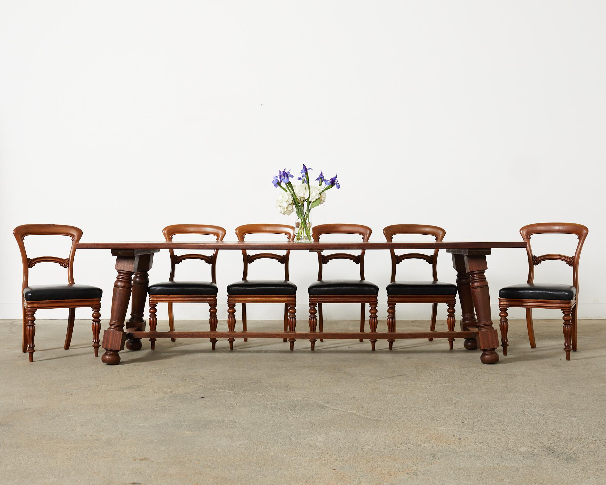 Grand set of twelve 19th century William IV dining chairs crafted from mahogany. The chairs feature a gracefully curved crestrail with a scrolled splat. The generous seats are covered with dramatic black leather hides. The chairs are supported by
