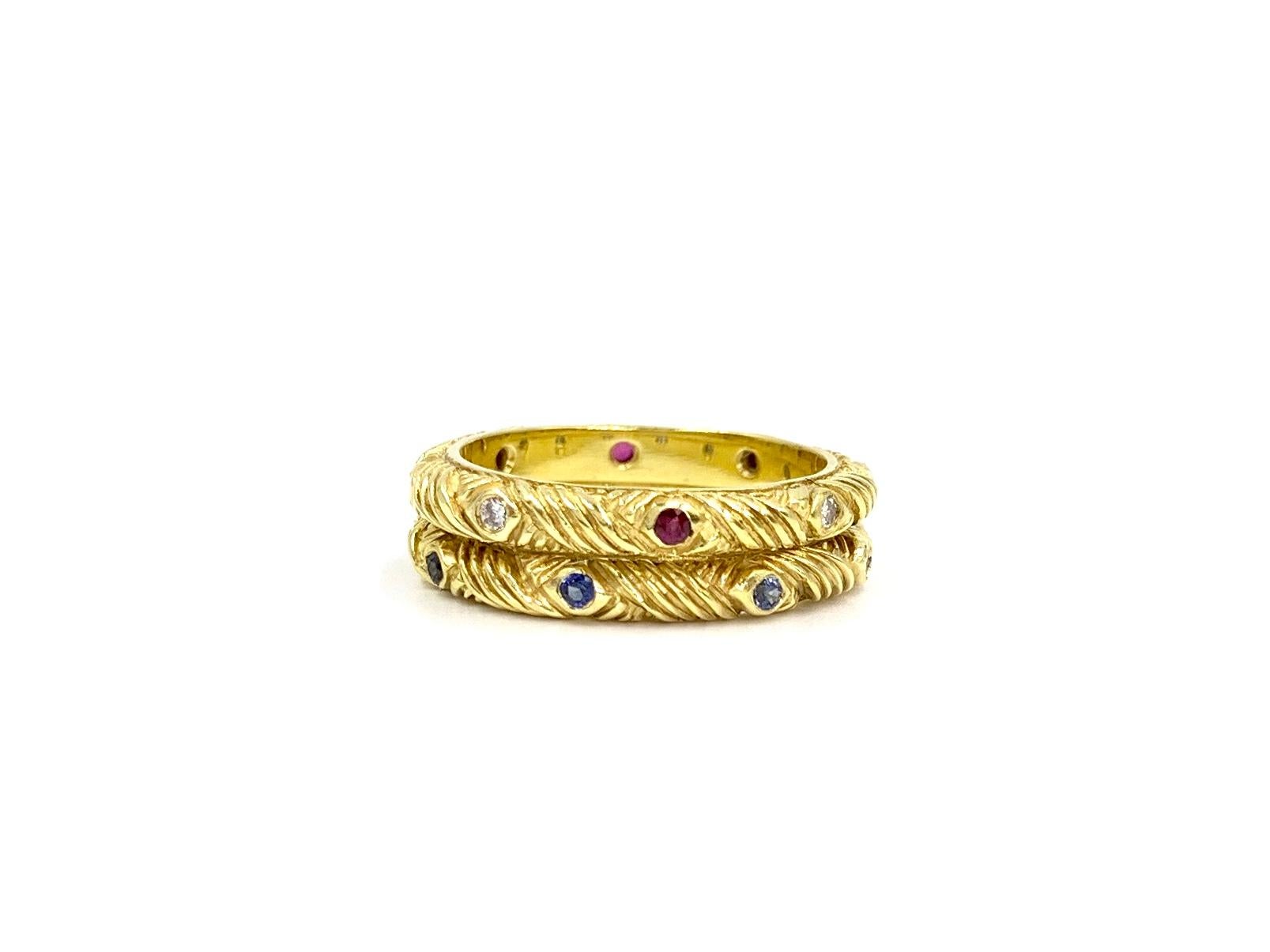 Set of two hand carved 18 karat yellow gold stackable 3mm band rings by JJ Marco. One band features 8 blue sapphires at .20 carats total weight. The other band features alternating diamonds and rubies with .08 carats of diamonds and .10 carats of