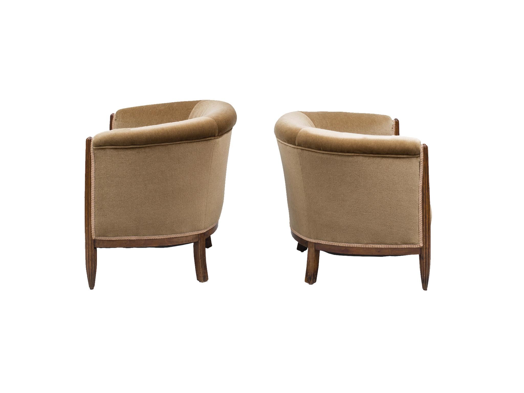 Two elegant Art Deco club chairs that are a near-pair. They were crafted in the 1930s, comprising of mahogany wood frame and legs. The fabric is a later re-upholstery work: a lovely mohair in a champagne-taupe hue. The front legs are fluted, while