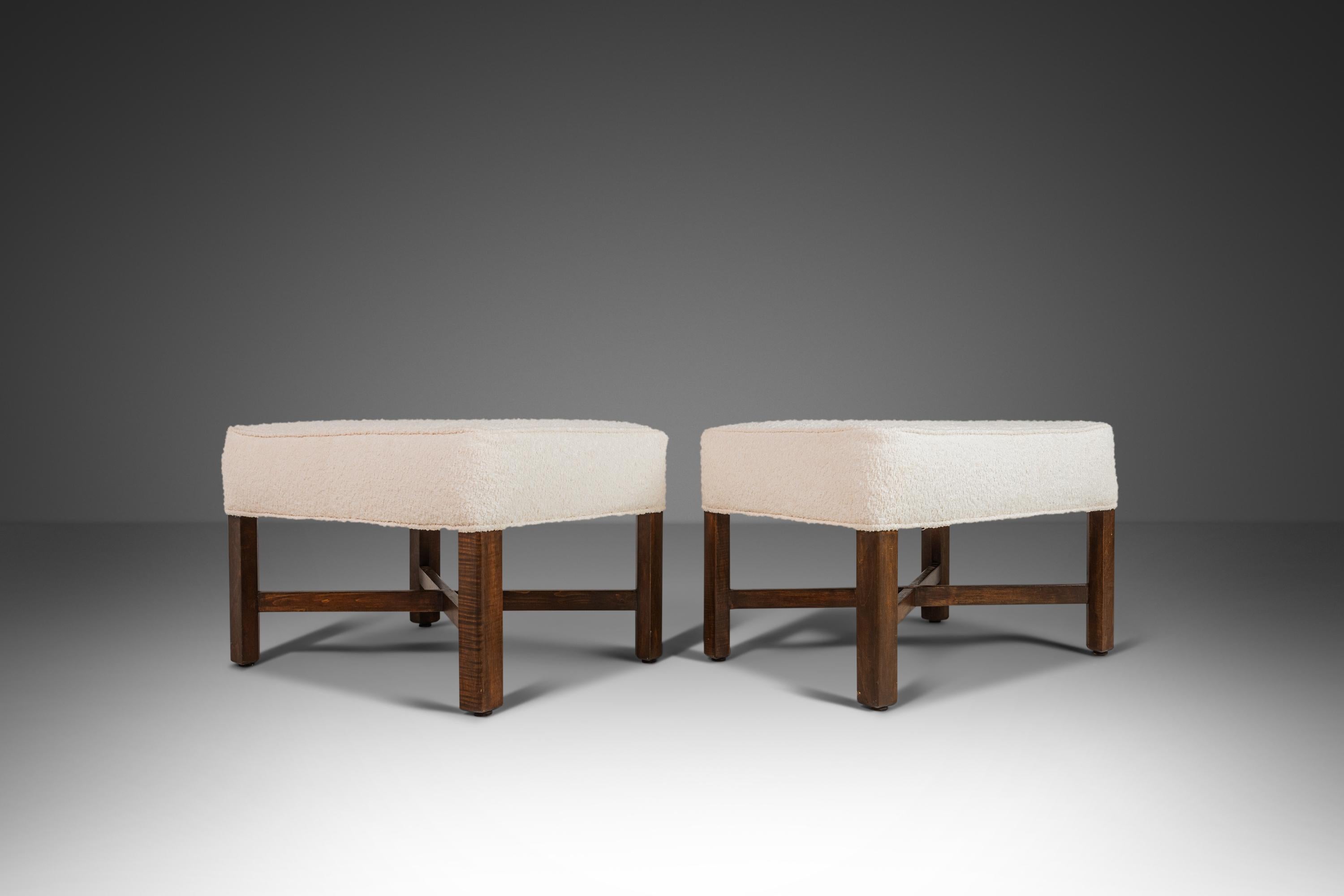 This is a pair of ottomans / footstools designed in the manner of Edward Wormley for Dunbar. The fabric has been newly upholsterd in Knoll Fabrics white bouclé. The wooden walnut base has a striking cross legged design. circa