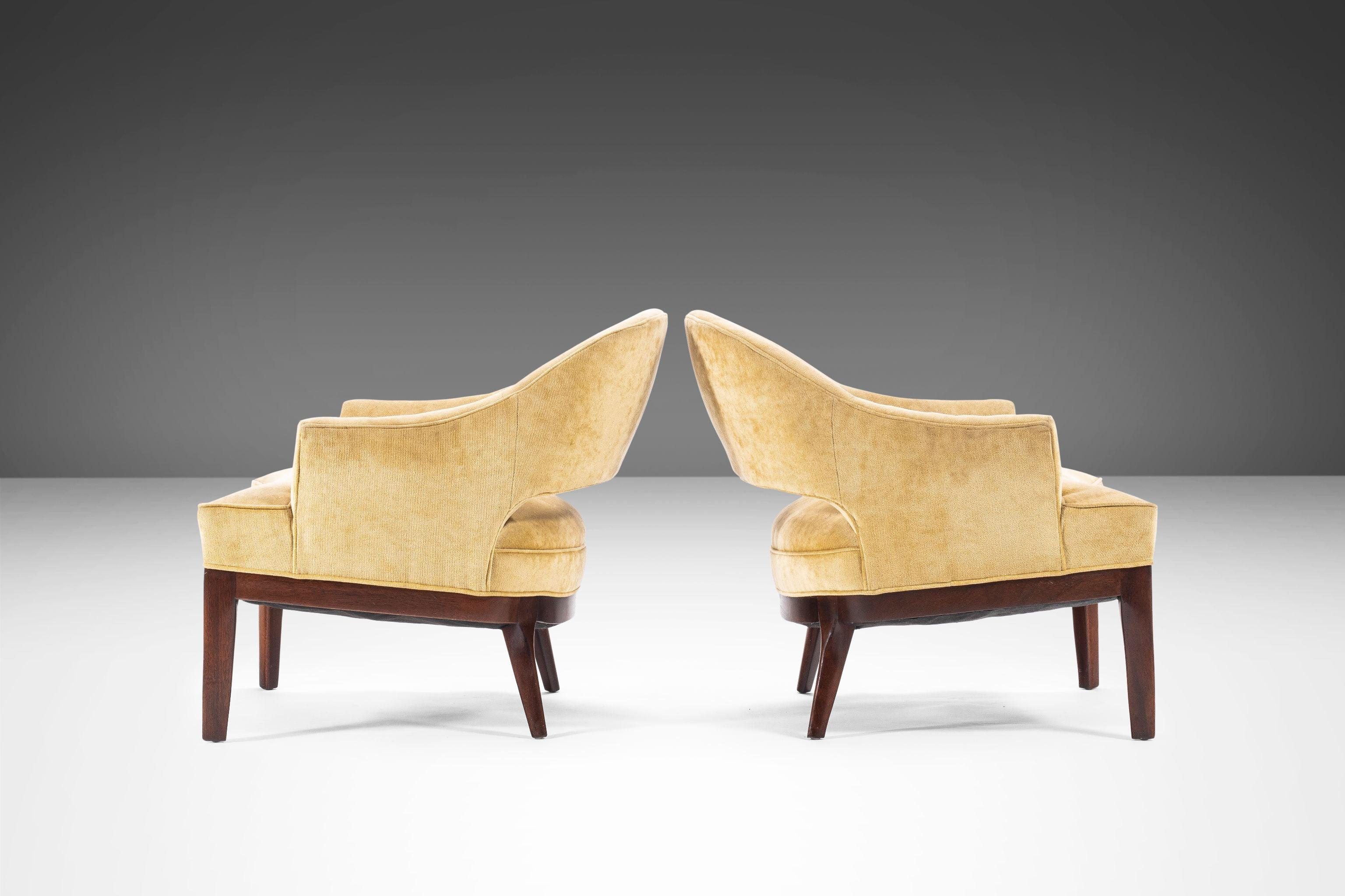 Set of two Mid-Century Modern low slung club chairs attributed to Harvey Probber. Chairs feature sculpted walnut legs with a curved sabre-shaped faces, and stunning original microfiber fabric in a neutral cream color. Perfect in both a home or