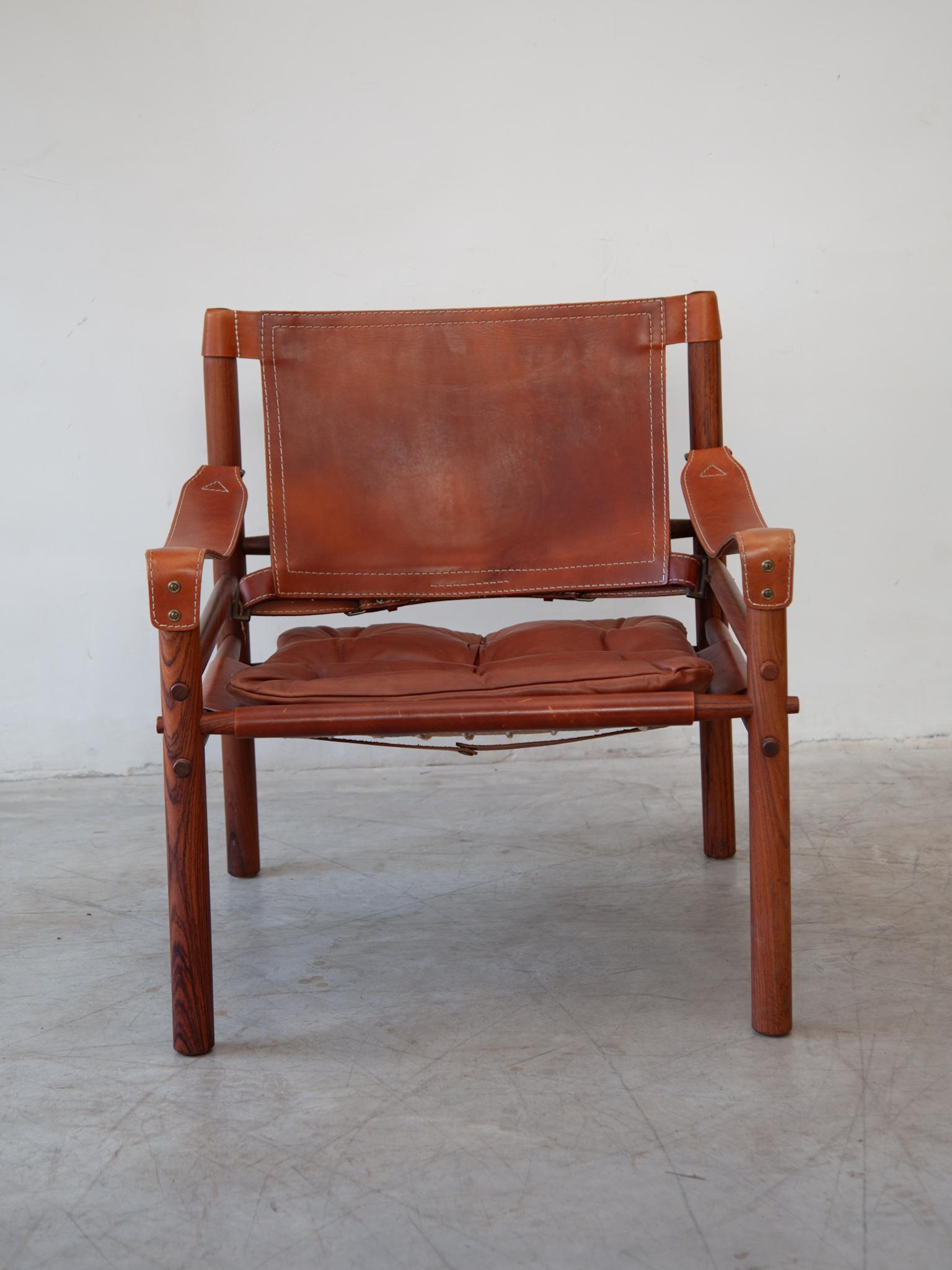 Beautiful original model of a modern classic safari chair. A set of two Sirocco arm chairs designed by Arne Norell in 1964, Sweden. Frame in solid wood, armrests, backrest and seat in thick brown leather with a very nice patine by use. This model is