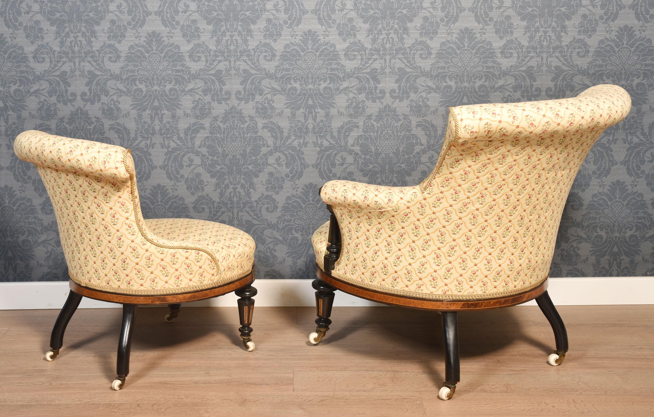 Un ensemble de chaises de chambre à coucher pour deux personnes. Les cadres en ébène et incrustés d'Amboyna ont des dossiers rembourrés en forme et des sièges surchargés. Le tout est surélevé sur des pieds flûtés se terminant par des roulettes en