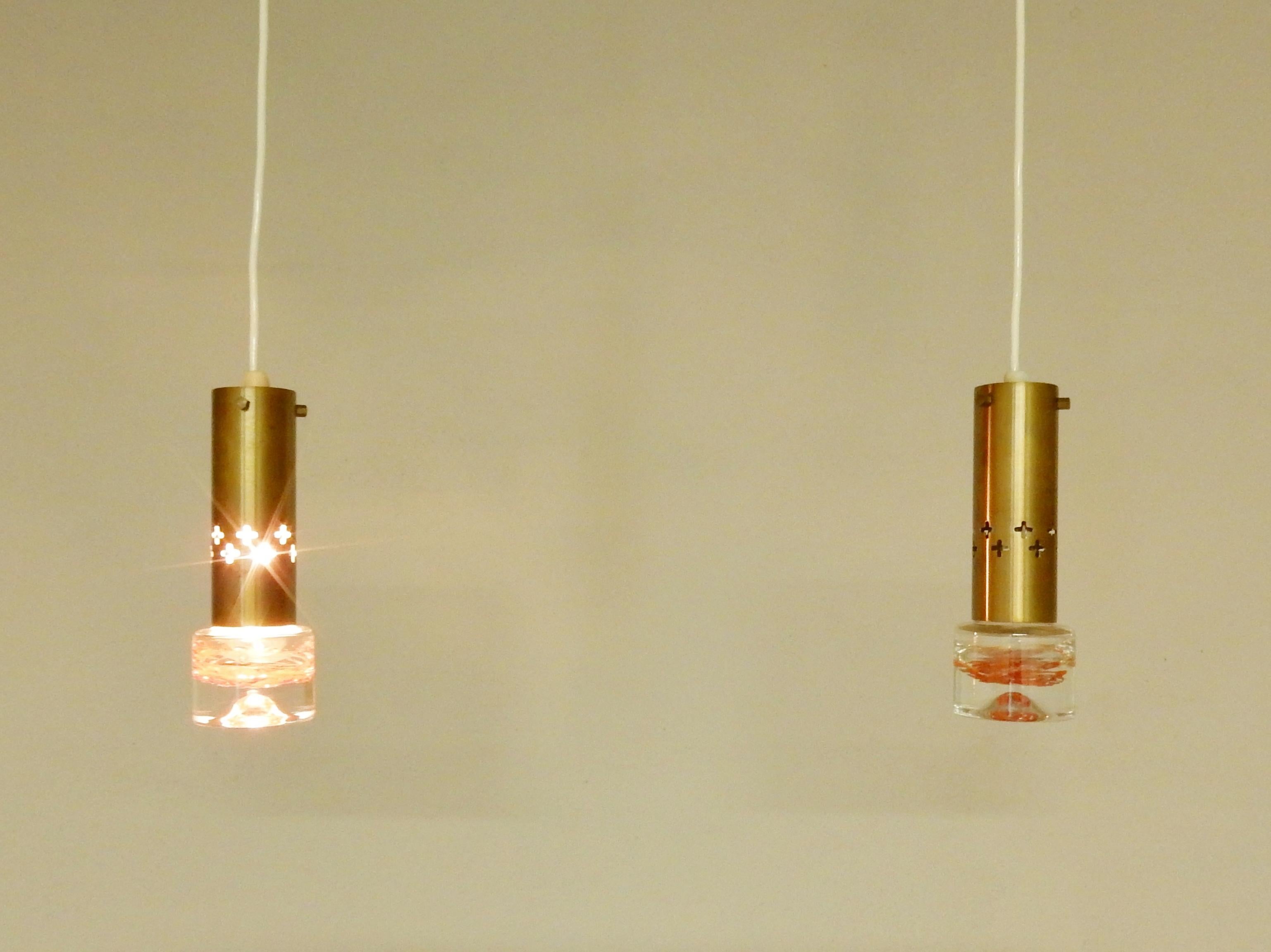 This very nice set of two pendant lights was designed for the Swedish lighting manufacturer Örsjö Belysning in the 1960's. The brass is decorated with two rows of crosses and hexagon fasteners to the suspension. The glass is soft do to the round