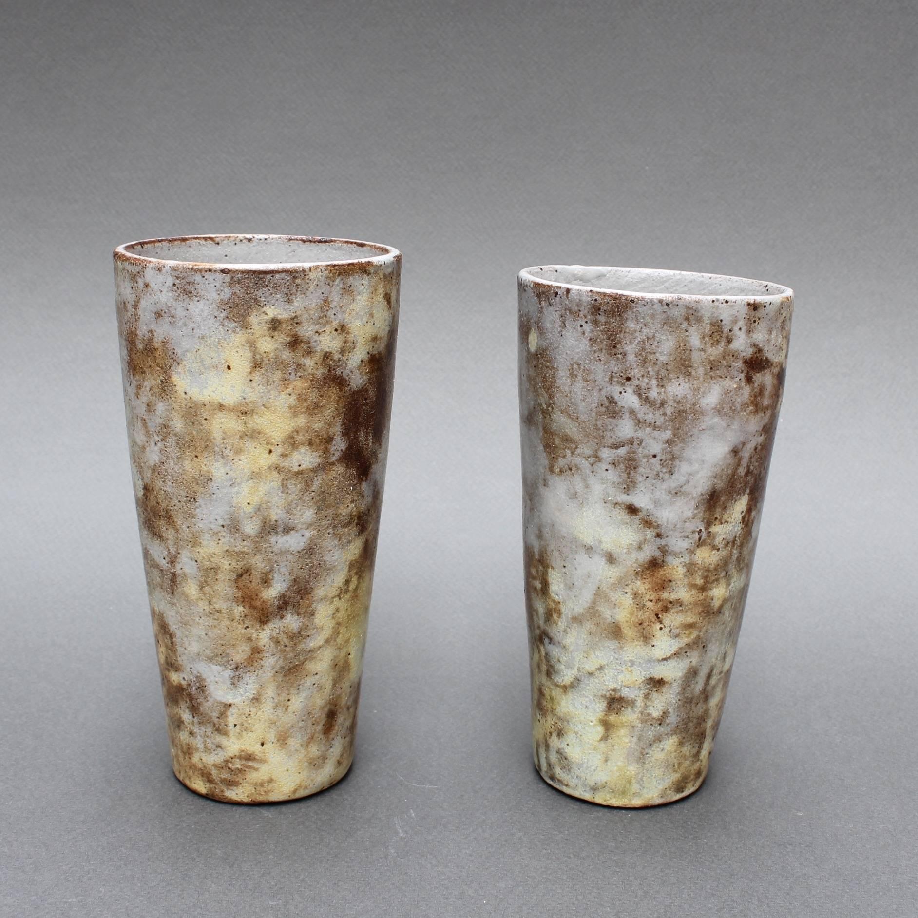 Set of two ceramic vases/cups by Alexandre Kostanda (circa 1960s). This pair of beautiful vessels - one slightly shorter than the other - present a misty appearance with earth tones in brown, beige and delicate yellows. They may be displayed