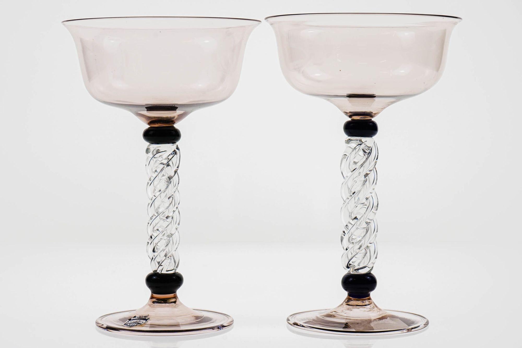 Rare set of two champagne glass with amethist bowl and foot, black neck and pillar stem in solid clear glass twisted.
A sculptural set. Dated on the 50s-60s due to the change of style for champagne use on the later decades.