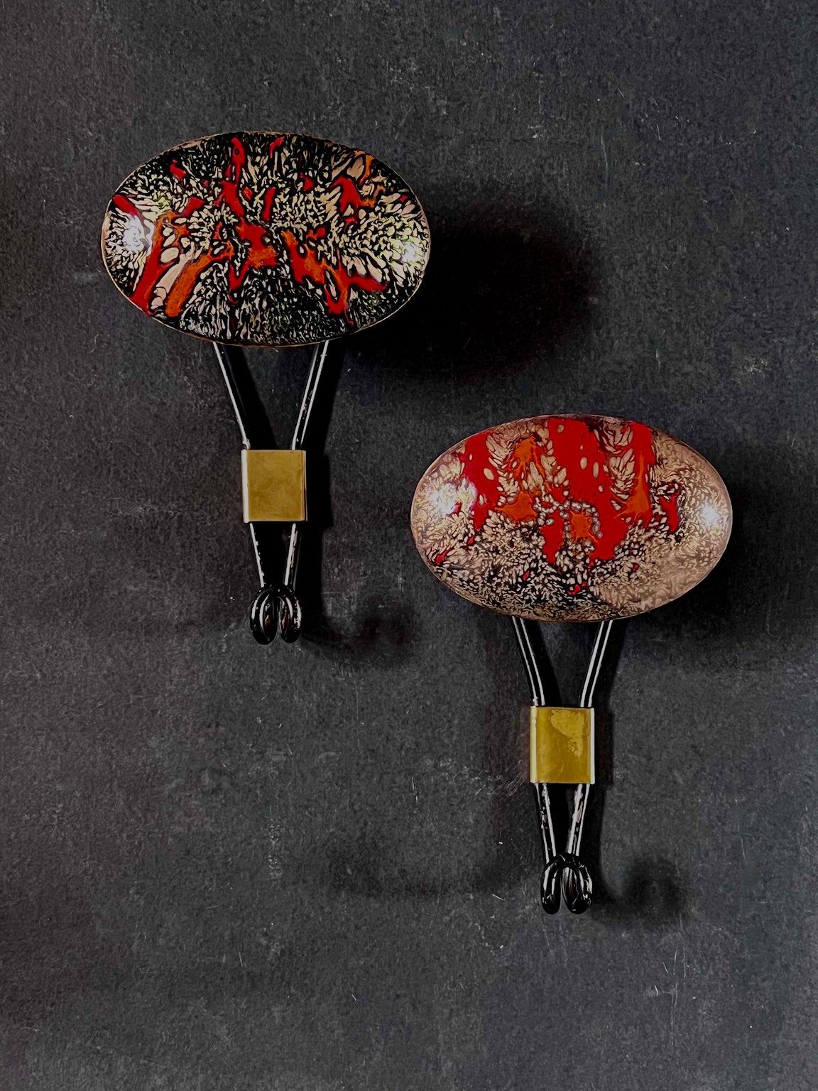 A set of two large handmade coat hooks decorated with enamel. Italy, mid-20th century.

Each piece comprises a black metal frame with a hook below and a decorative, domed enamel hanging point above. The enamel is nicely made in tones of red and