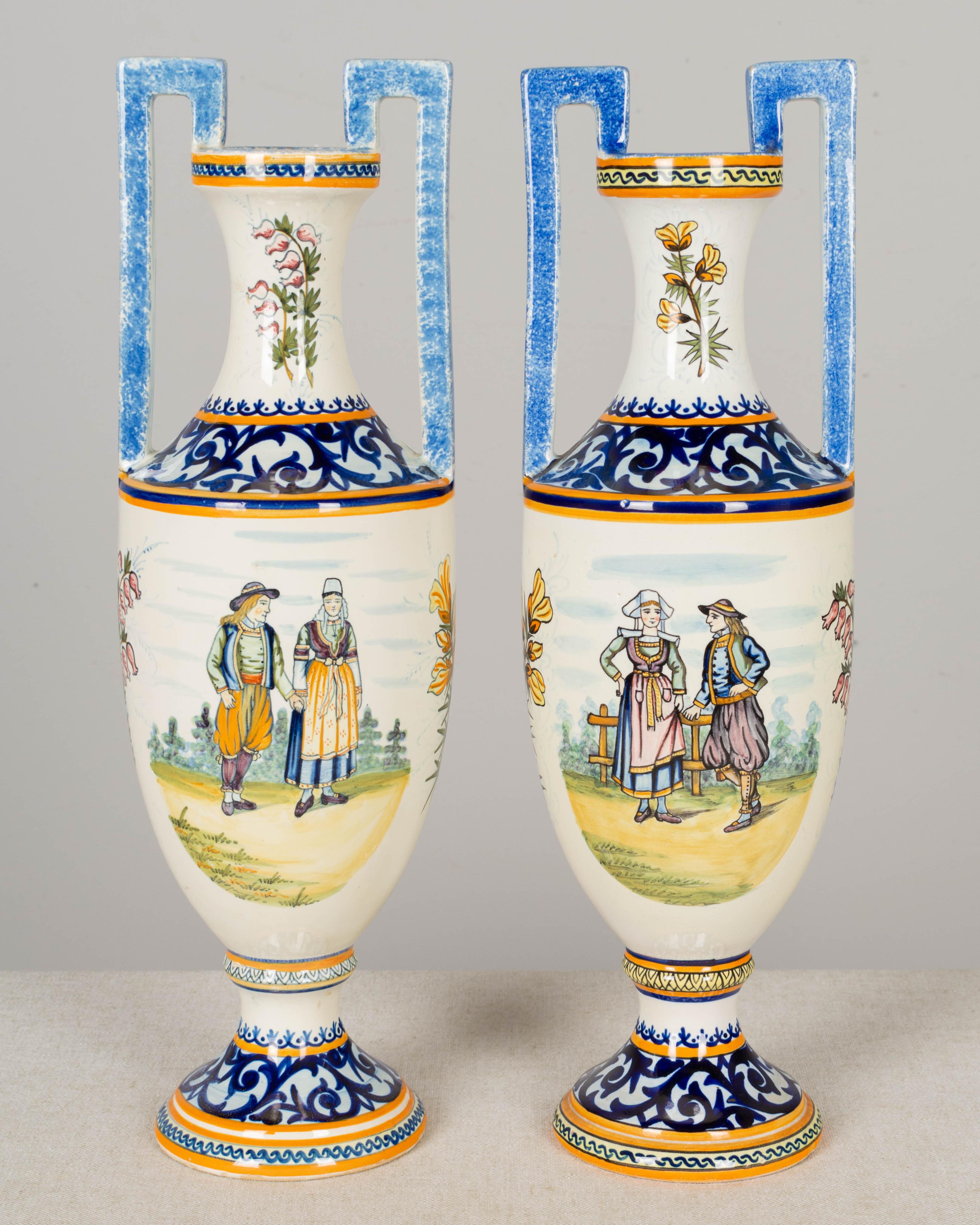 A set of two of French faience vases by Henriot Quimper, hand-painted with a man and woman depicted in traditional country attire in a pastoral setting. The reverse side each vase has an armorial crest, one with the crest of Bretagne and the other