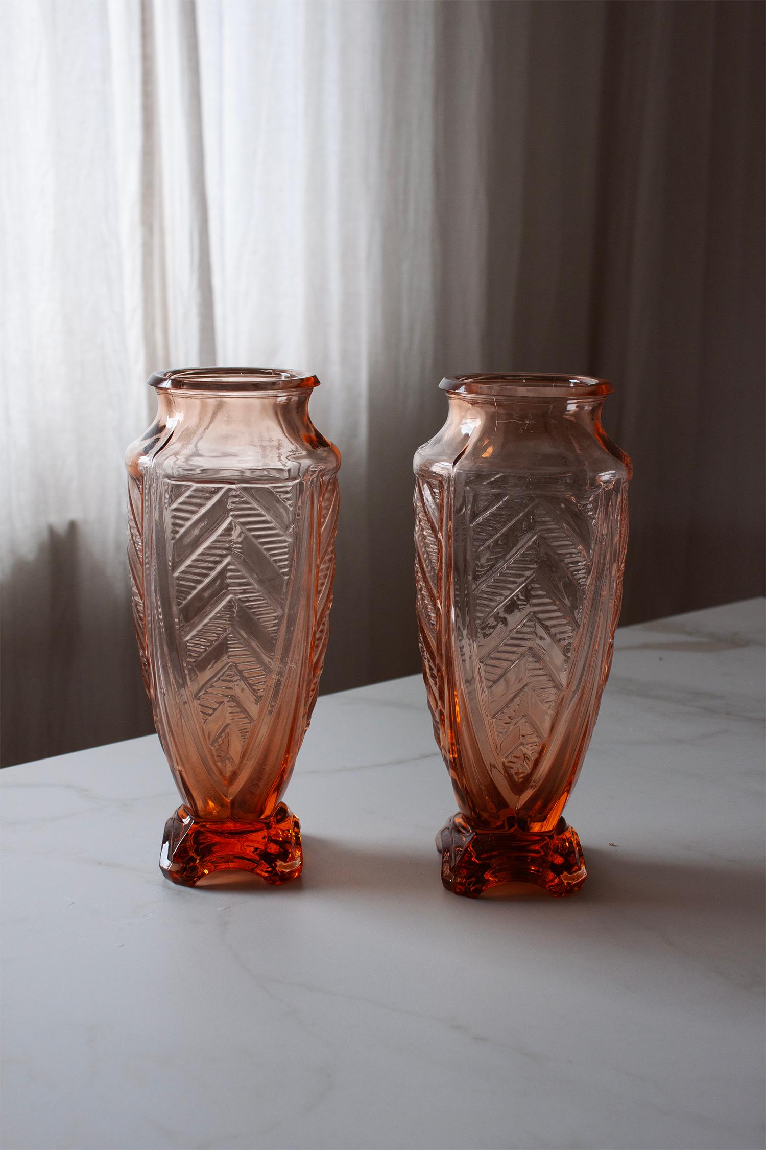 This set of two Art Deco glass vases exudes timeless elegance and vintage charm. Each piece features a beautifully crafted geometric relief pattern, reflecting the iconic aesthetic of the Art Deco era. The soft rose-tinted glass subtly diffuses
