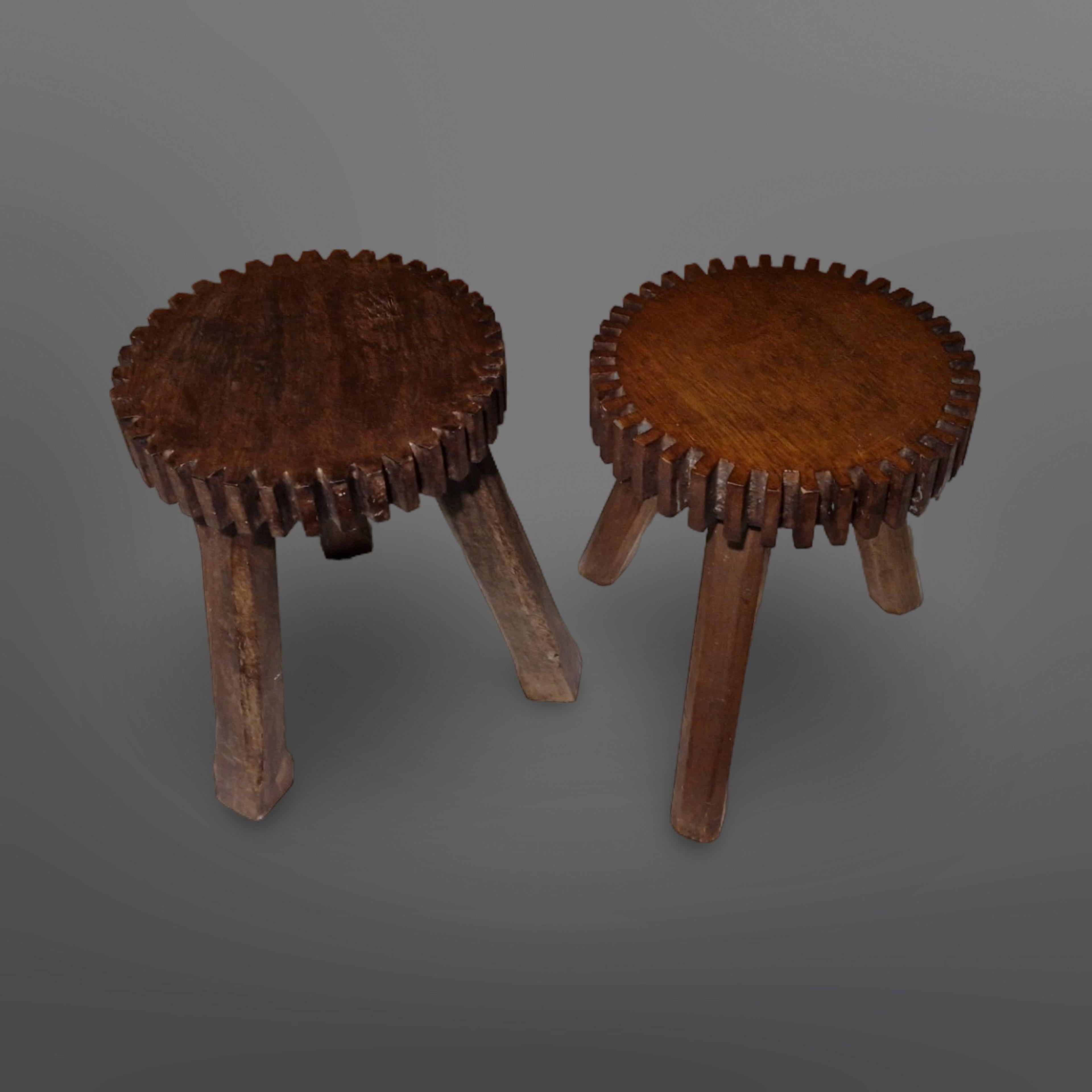 Handmade set of two brutalist stools. Hand carved from solid wood. The seats have serrated edges resembling industrial cogs. They differ slightly in size accentuating the handmade characteristics. 
The dark stained wood gained a patina through the