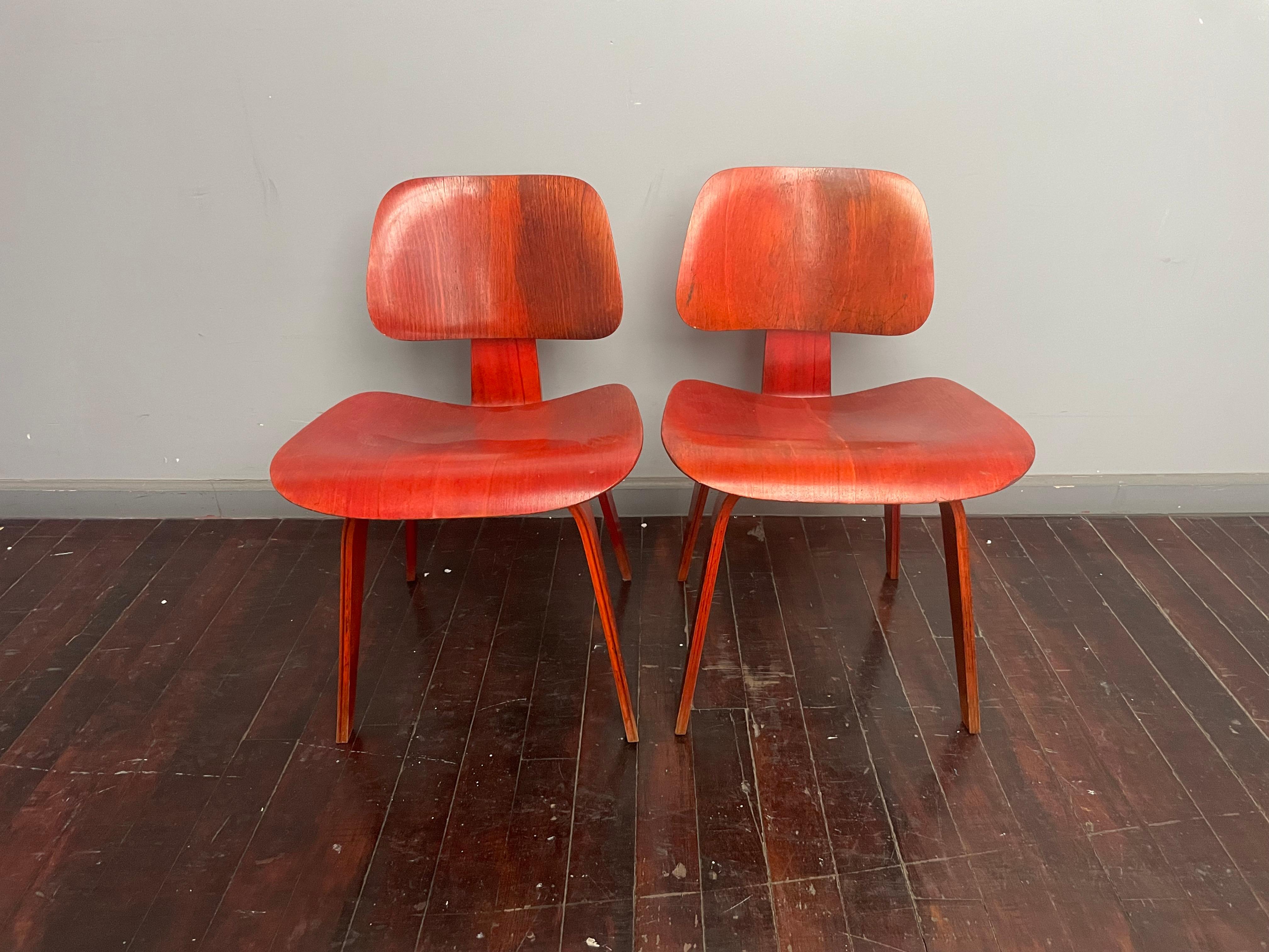 Presenting a rare pair of early edition Eames DCW chairs in red aniline dye. Both chairs retain the desirable Evans label, indicating these chairs were manufactured before 1950. 

Chairs show beautiful patina. 