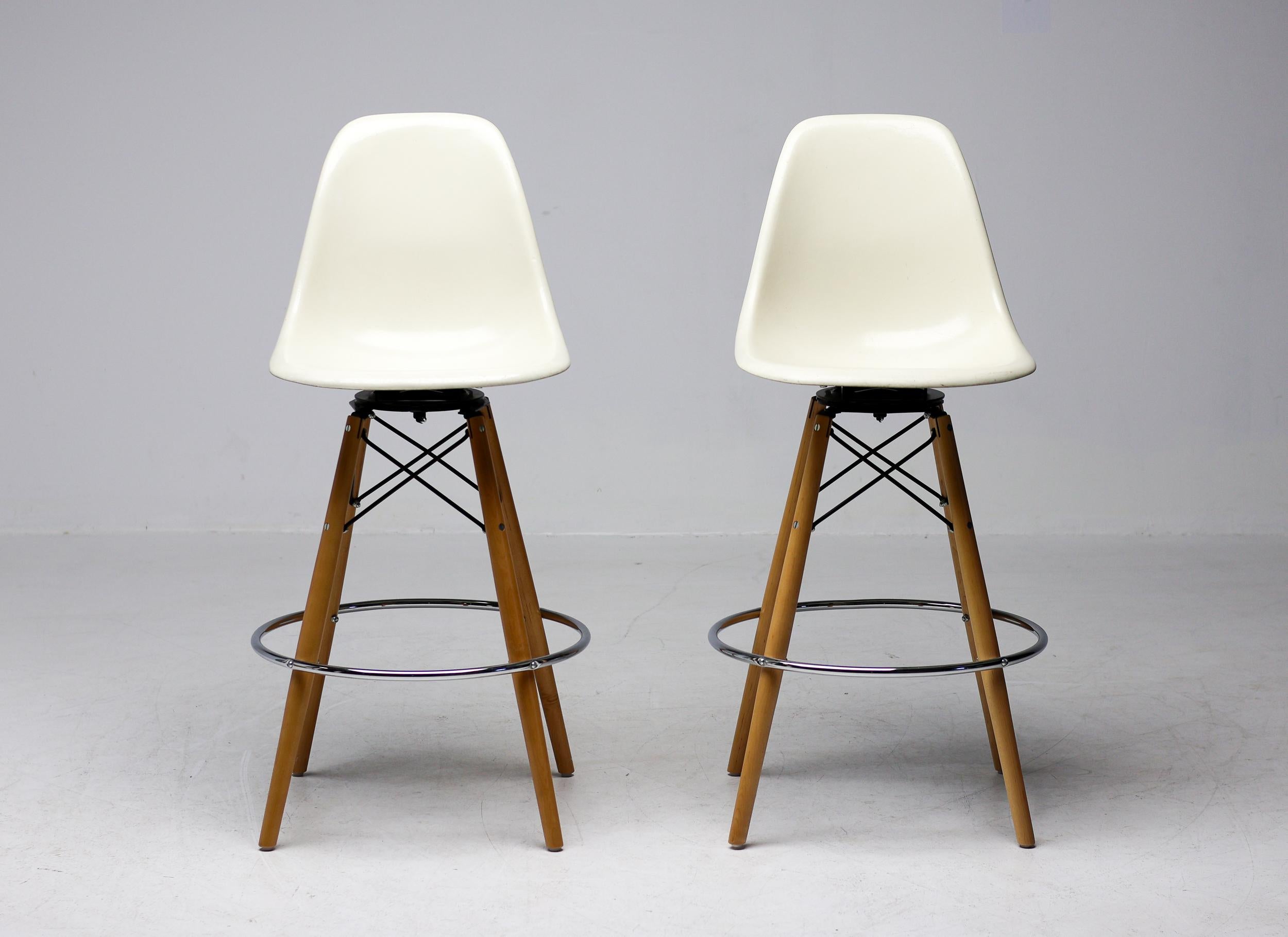 Beautiful pair of barstools designed by Charles & Ray Eames in off-white fiberglass with a maple swivel dowel base. 
The stools are marked with the embedded Herman Miller logo underneath the seat, designating it as a USA production, circa 1980.
The