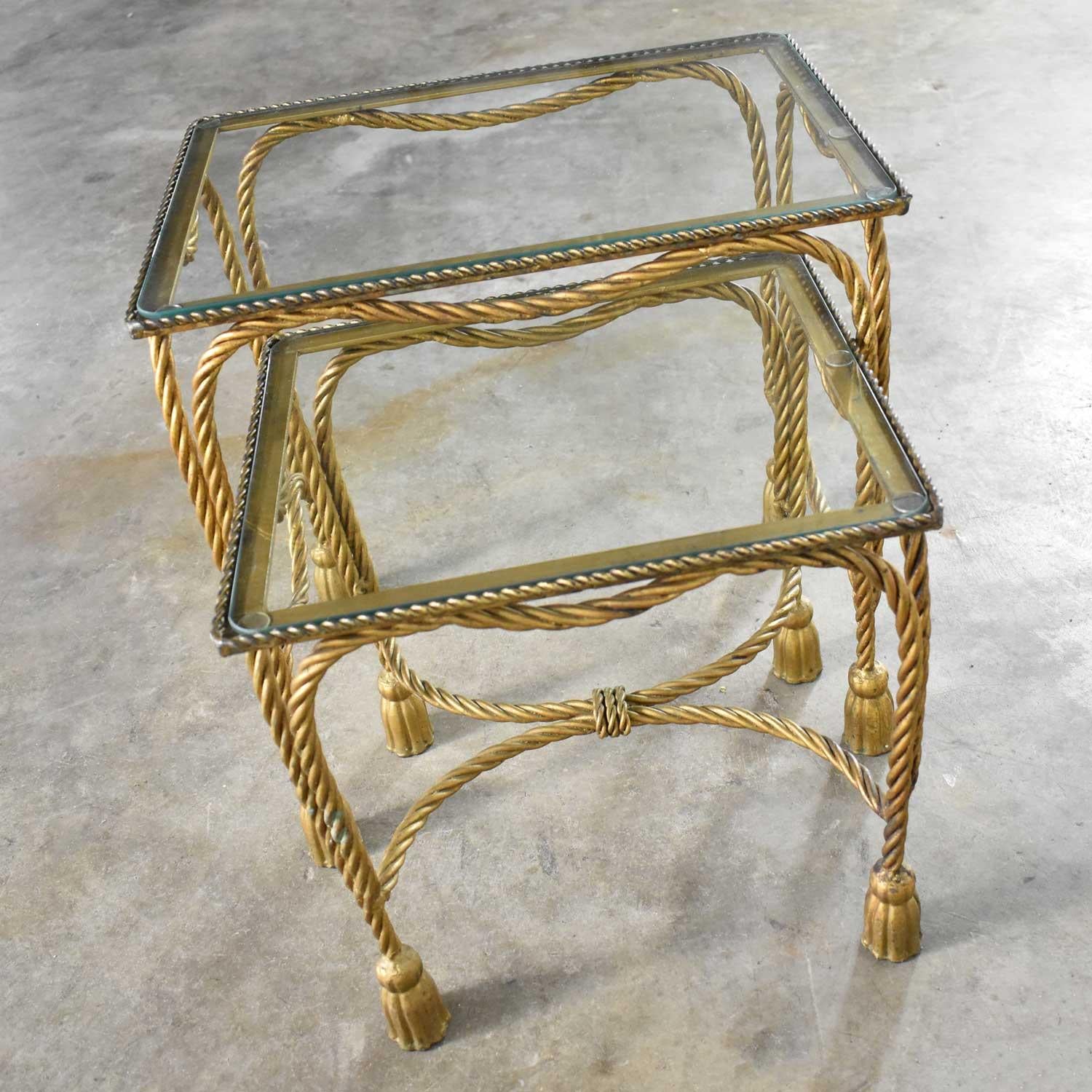Beautiful set of two Hollywood Regency gilt rope and tassel nesting tables with glass tops. They are in wonderful vintage condition with no outstanding flaws that we have seen. They do have normal wear for their age. The gilding has a nice age
