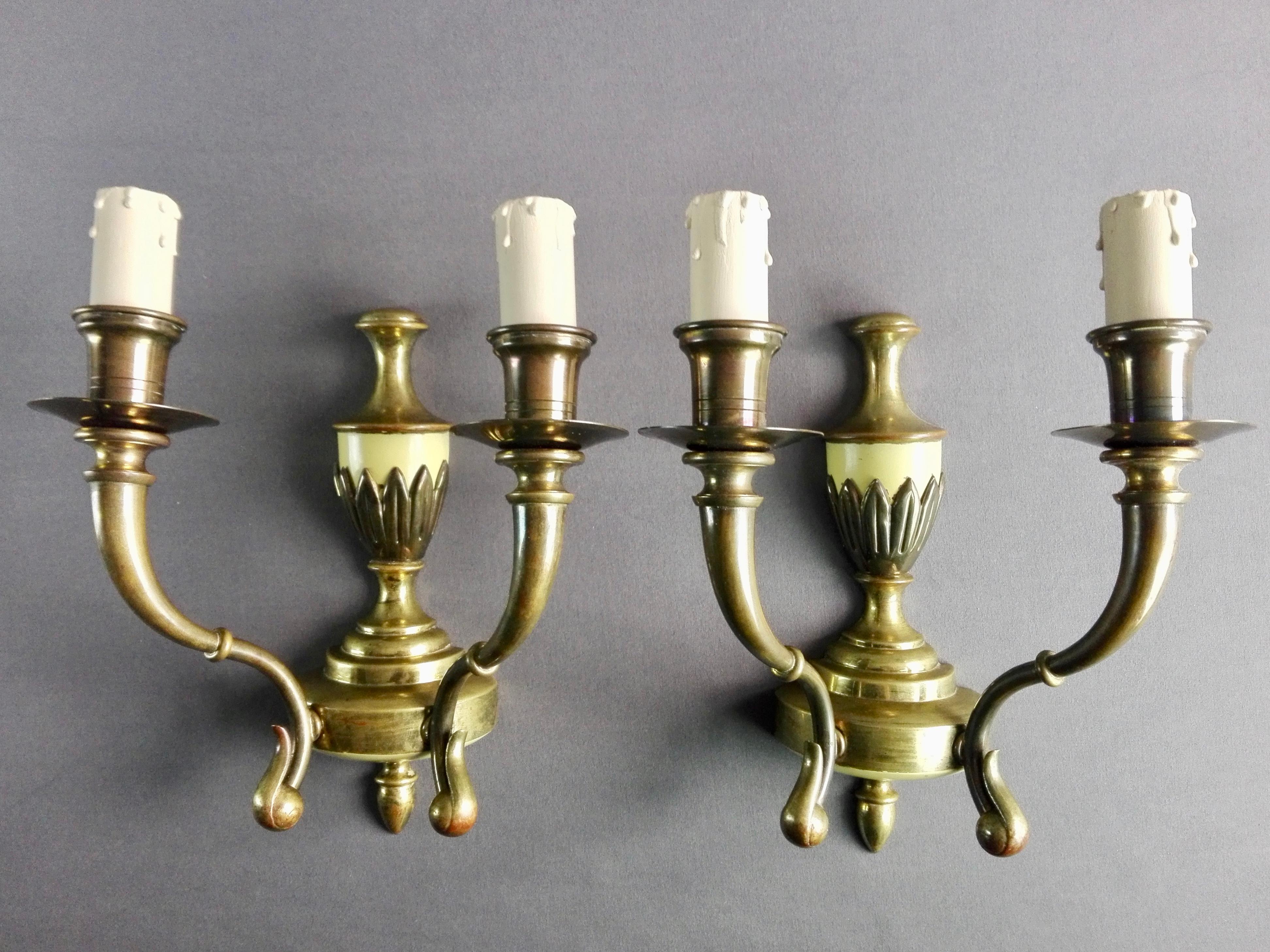 Pair of late 1940s - early 1950s Italian two-light sconces. The structures are in solid brass with ivory-yellow lacquered details and original wooden candle lampholders. 
Lamps have been completely disassembled to perform a thorough cleaning using