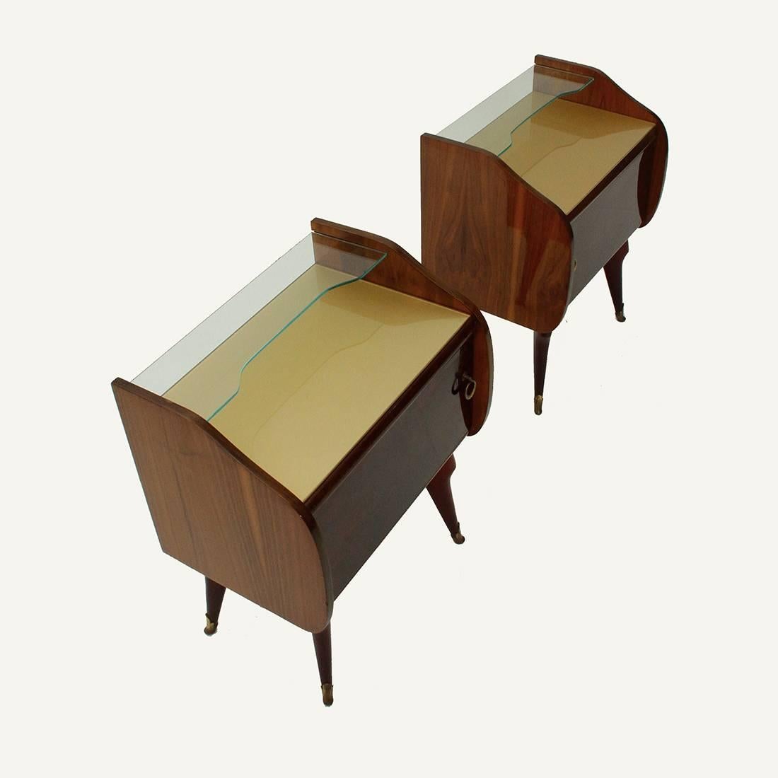 Pair of bedside tables of Italian production from the 1950s.
Wooden structure in veneered.
Compartment with brass handle.
Colored glass top, shaped glass top shelf.
Turned wooden legs with brass tips.
Good general conditions, some signs are