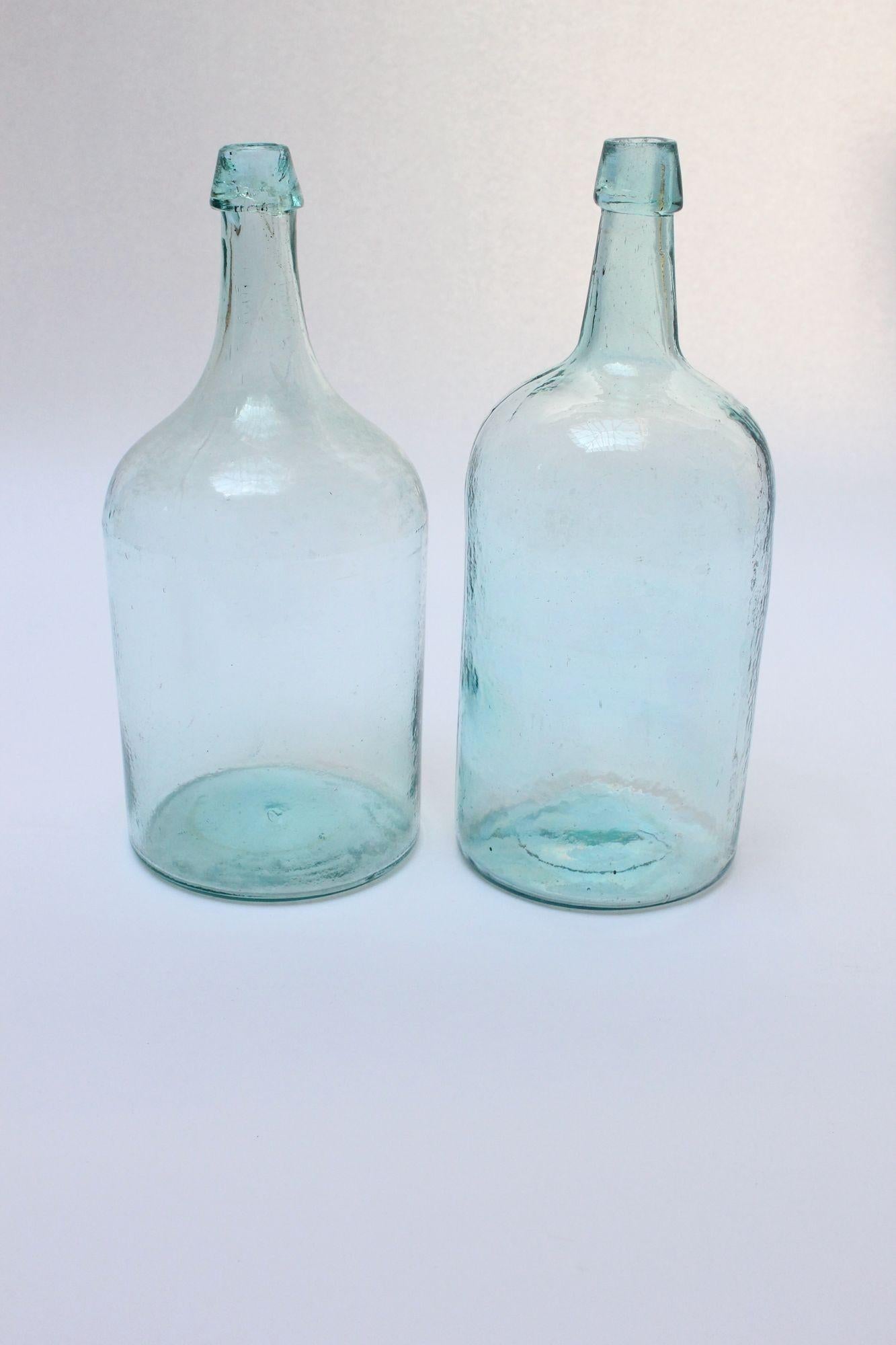 Set of two American ca. 1910 spirits/wine bottles, both aqua/turquoise tinted with hand-finished details. 
The one on the left was made via dip molding, evidenced by the glass discontinuity formed by the top of the dip mold. 
The one on the right