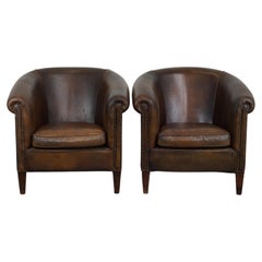 Set of two large, rugged, dark sheepskin leather club armchairs