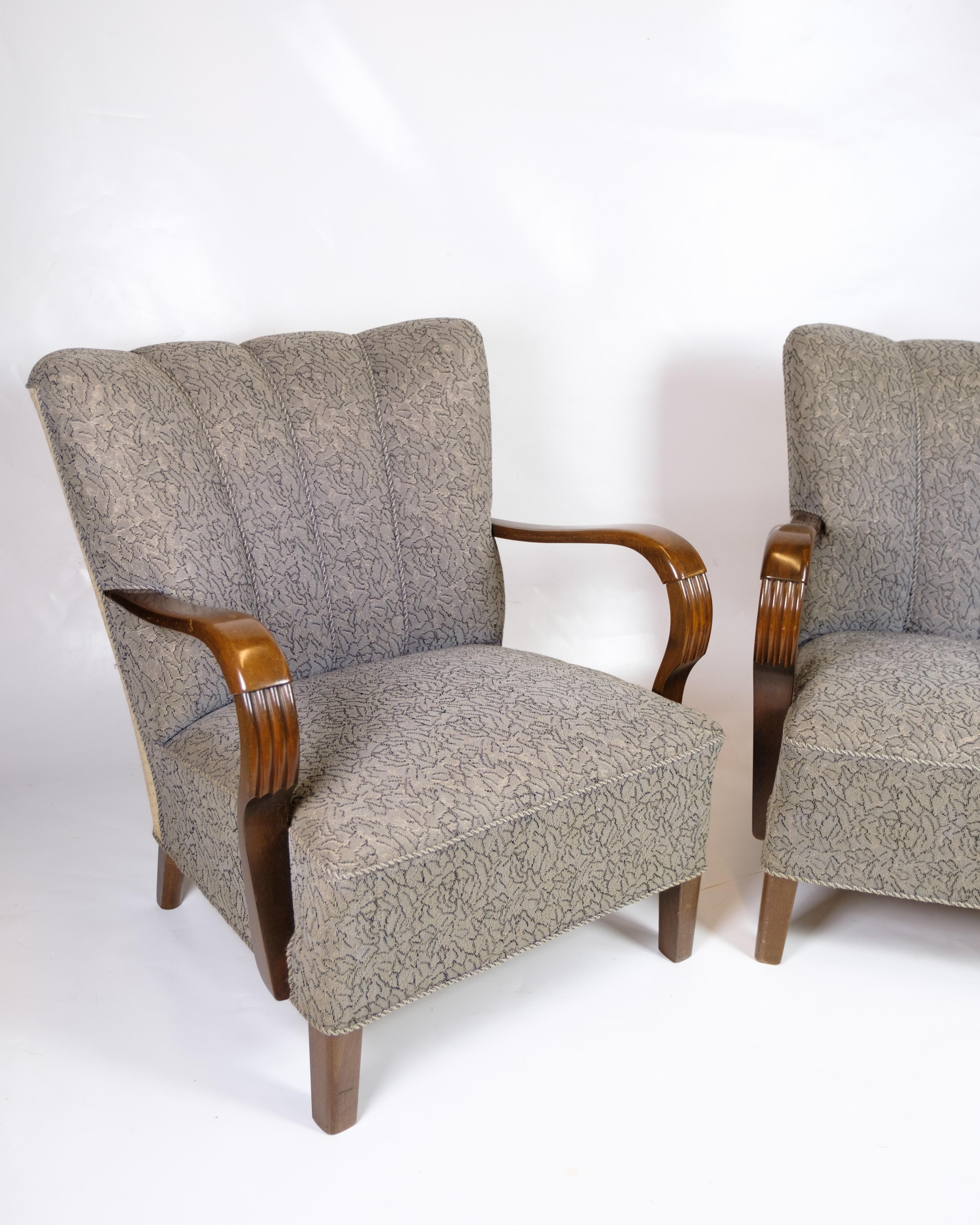 Set di 2 poltrone degli anni '60 con struttura e braccioli in legno scuro lucidato. Le sedie hanno uno schienale alto e padellato e ampi braccioli che offrono un buon sostegno. Sono rivestite in tessuto floreale e poggiano su solide gambe in legno.