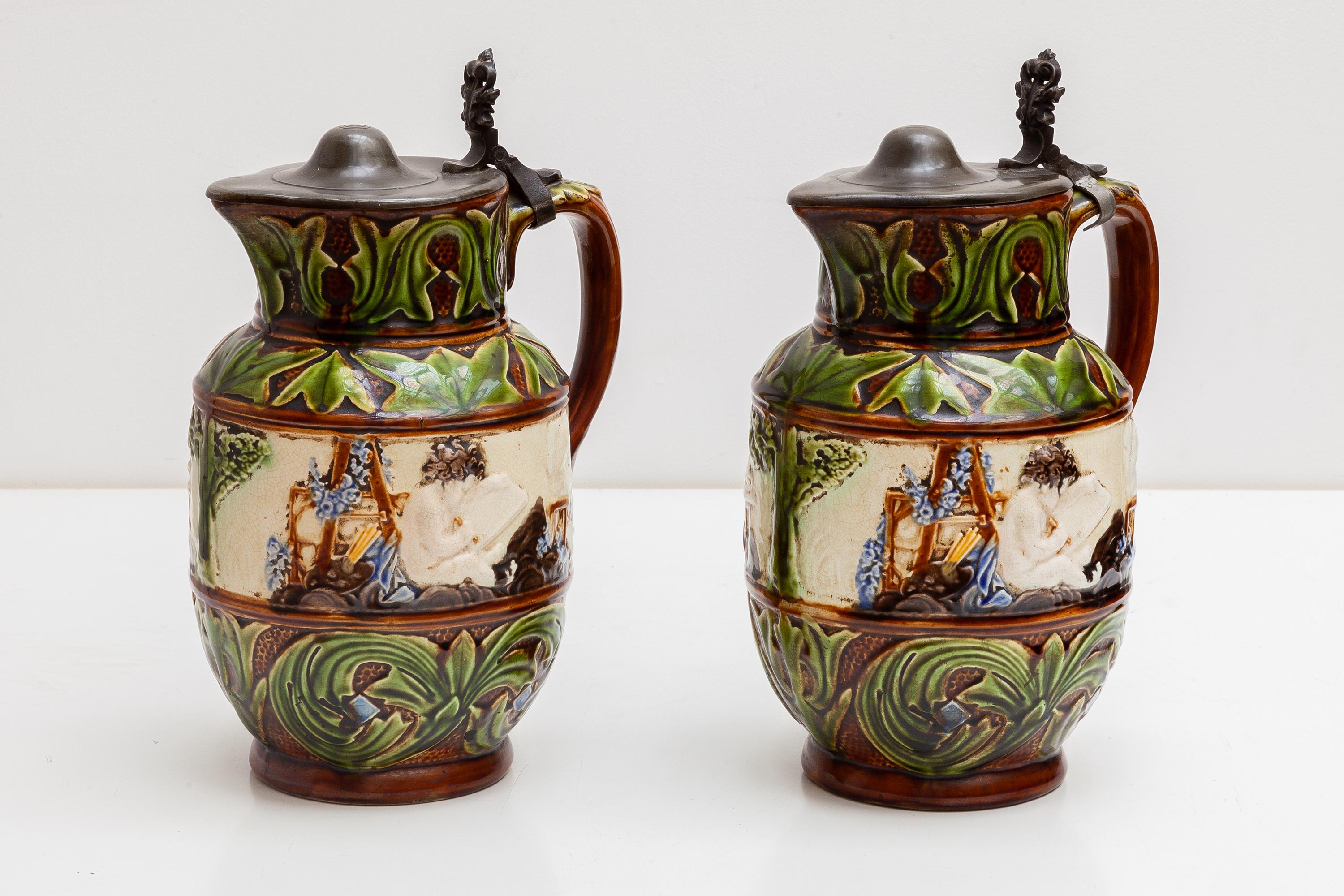 A set of 1851-1898 Belgium majolica pitchers, pottery jugs with pewter top.White hand painted cherubs sitting in a painting impression and accessories, at the bottom and at the top decorated with akanthos green leaves and trees.
Marks include