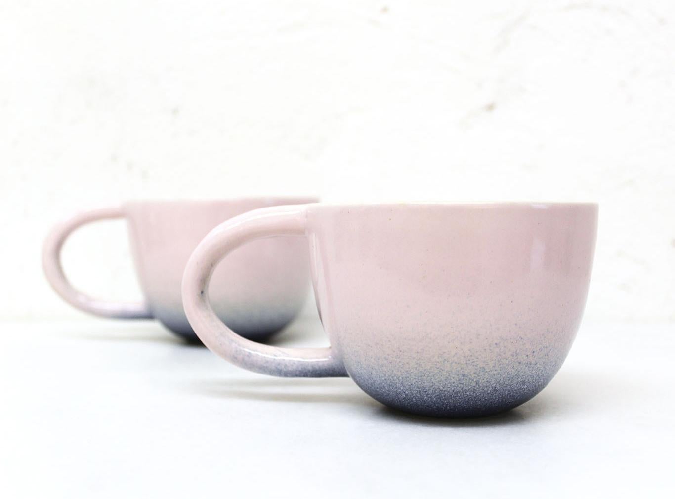 Set of two wheel-thrown white stoneware mugs with a modern spray glazed pink and indigo glossy glaze exterior with a matte satin white finish interior. 

Each mug approximately 6” x 4” x 3”.

Carol Joo Lee is an artist who loves working with