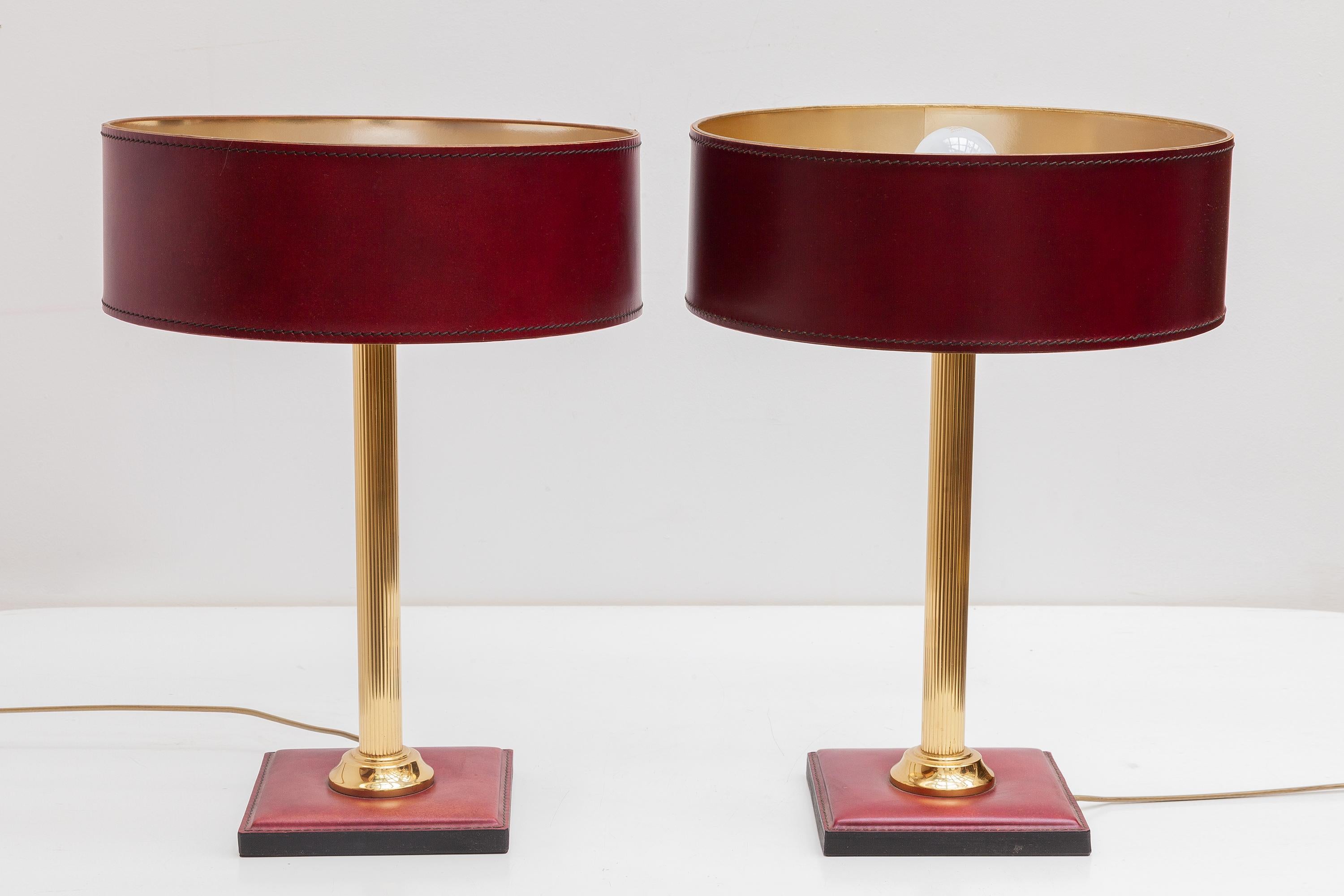 Set of two decorative table lamps in red leather attributed design by Jacques Adnet, France 1960. These leather clad table lamps has a square base and a brass stem with very nice hand-stitched shades in red leather. Beautiful in contrast with the