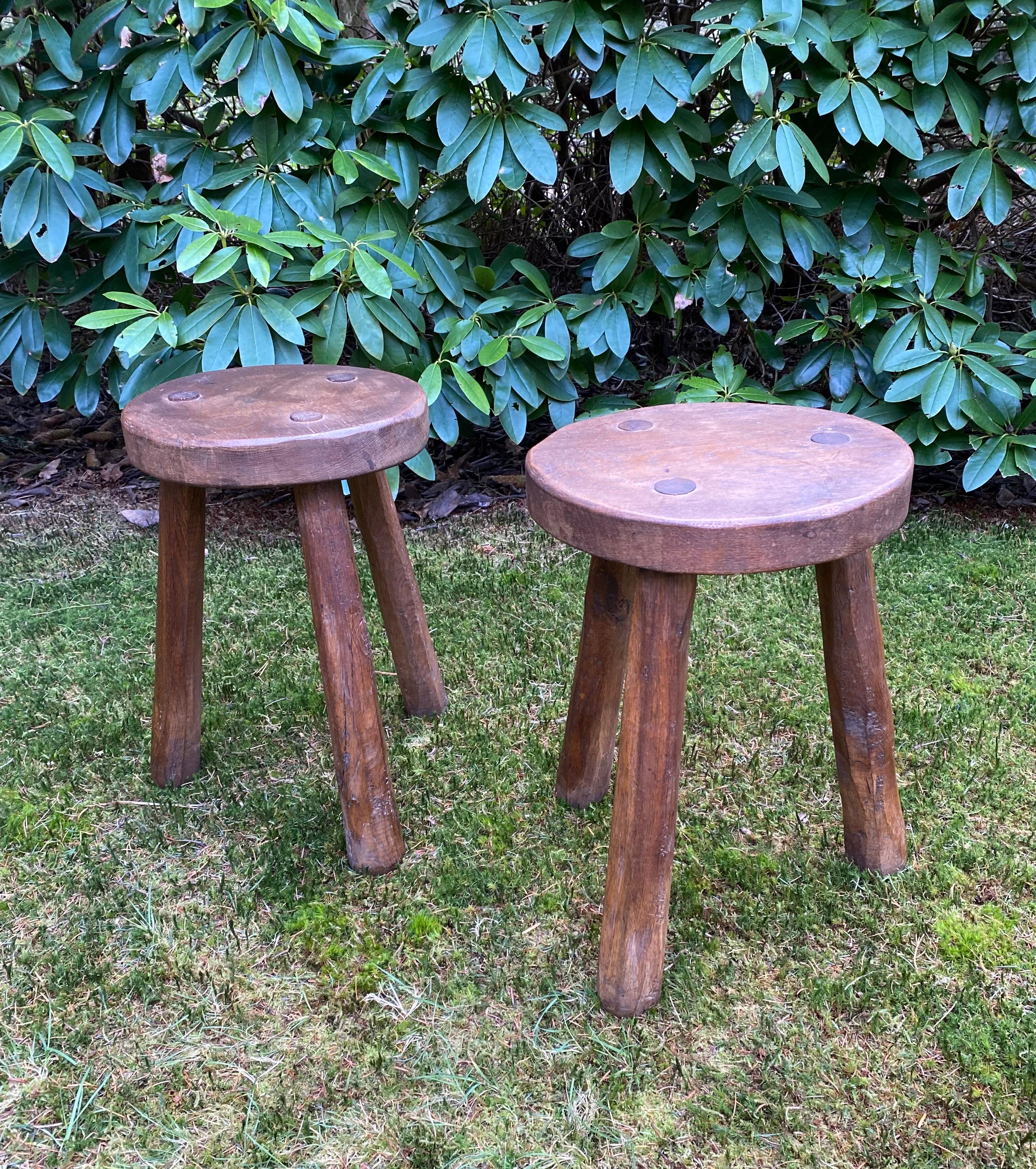 Stunning set of two rustic French Milking Stools, which were made out of  solid Oak wood. Similar to Charlotte Perriand. The stools feature a Tripod base and remain in good condition, with wear consisting with age and use, as to be seen on the