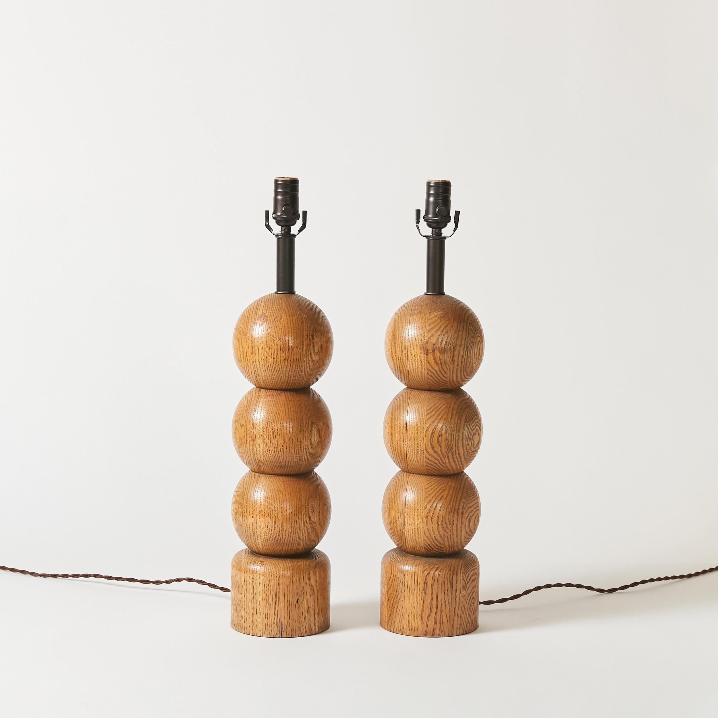 Set of two sculptural table lamps. Stacked wooden spheres resting on a pedestal. Original patina.
This item has been rewired with new hardware and braided cloth cord. This lamp does not include shade or harp.