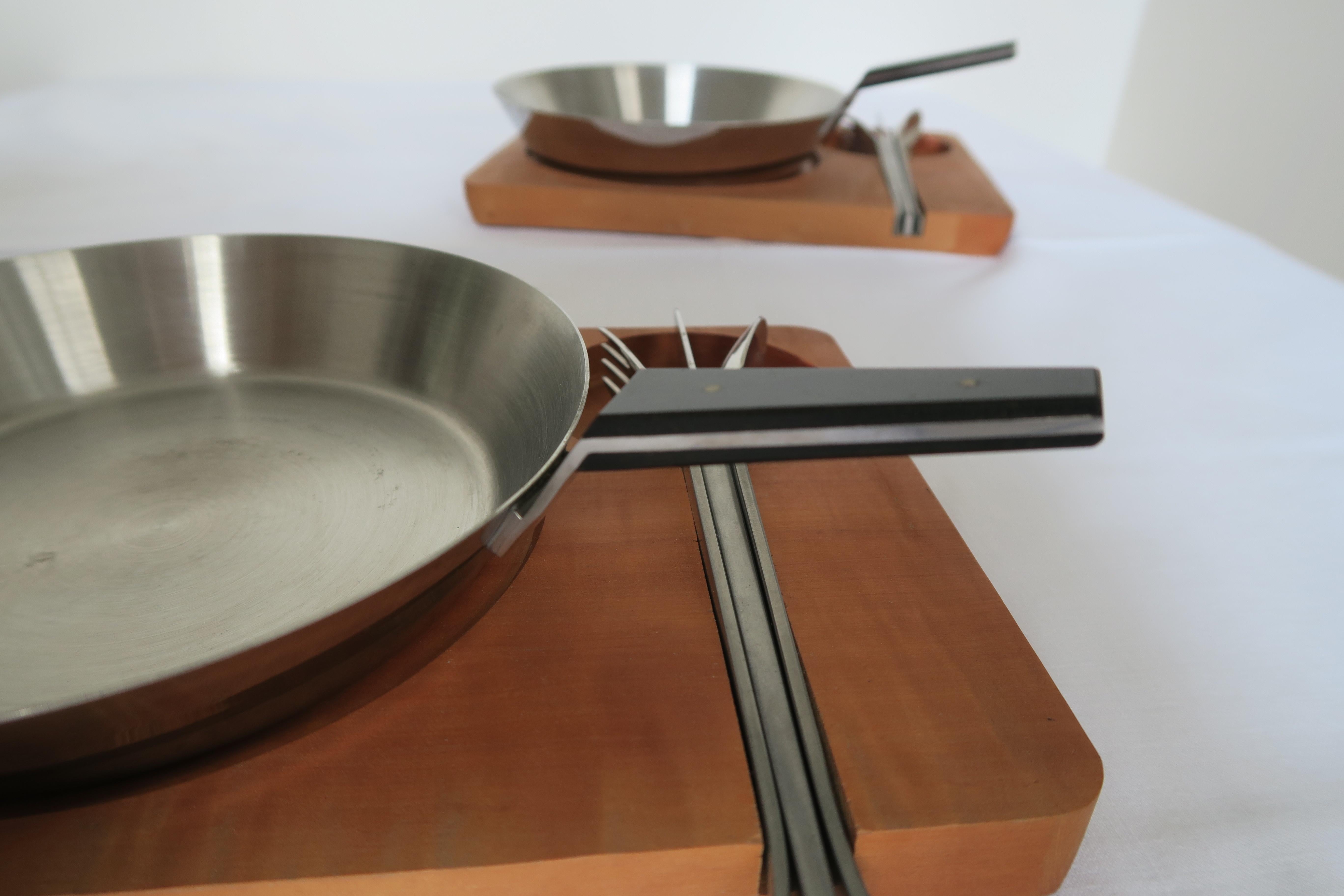 These two dining sets were designed and executed by the Austrian Werkstätte Carl Auböck. They date back to the 1950s and were crafted using the finest materials. In this case the trays are made of medium-dark wood, pans and cutlery are made of
