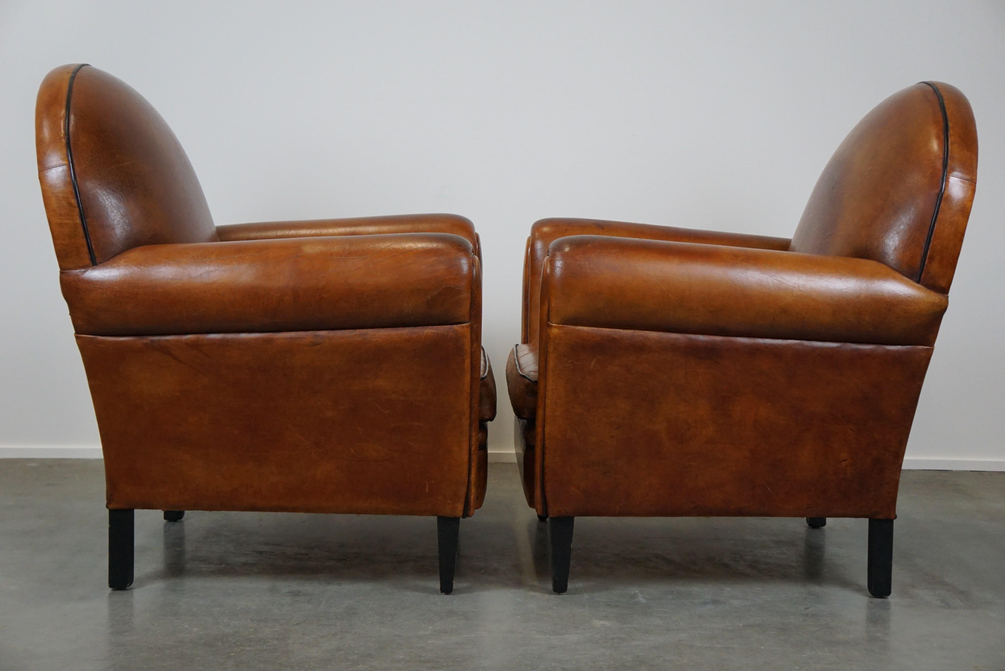 Offered by ByThijs, this delightful set of two sheep leather Art Deco style design armchairs with a beautiful patina and a positively used appearance. These armchairs don't hide the fact that they've lived a life; they proudly wear their life