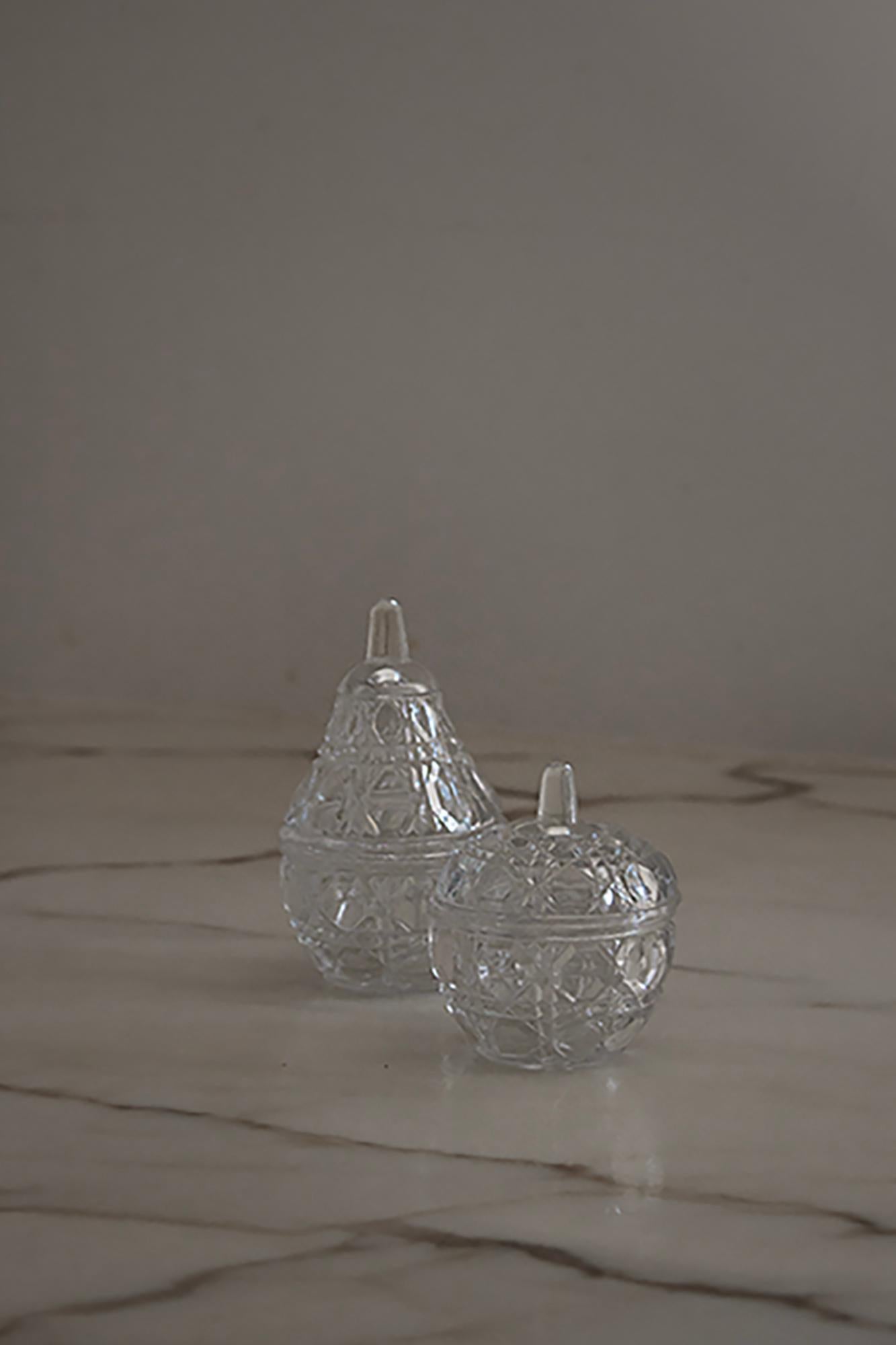 A set of vintage-inspired crystal containers. Crafted in the shapes of a pear and an apple, each piece features intricate geometric cut patterns that beautifully catch and reflect the light. Made from clear, high-quality glass, these charming