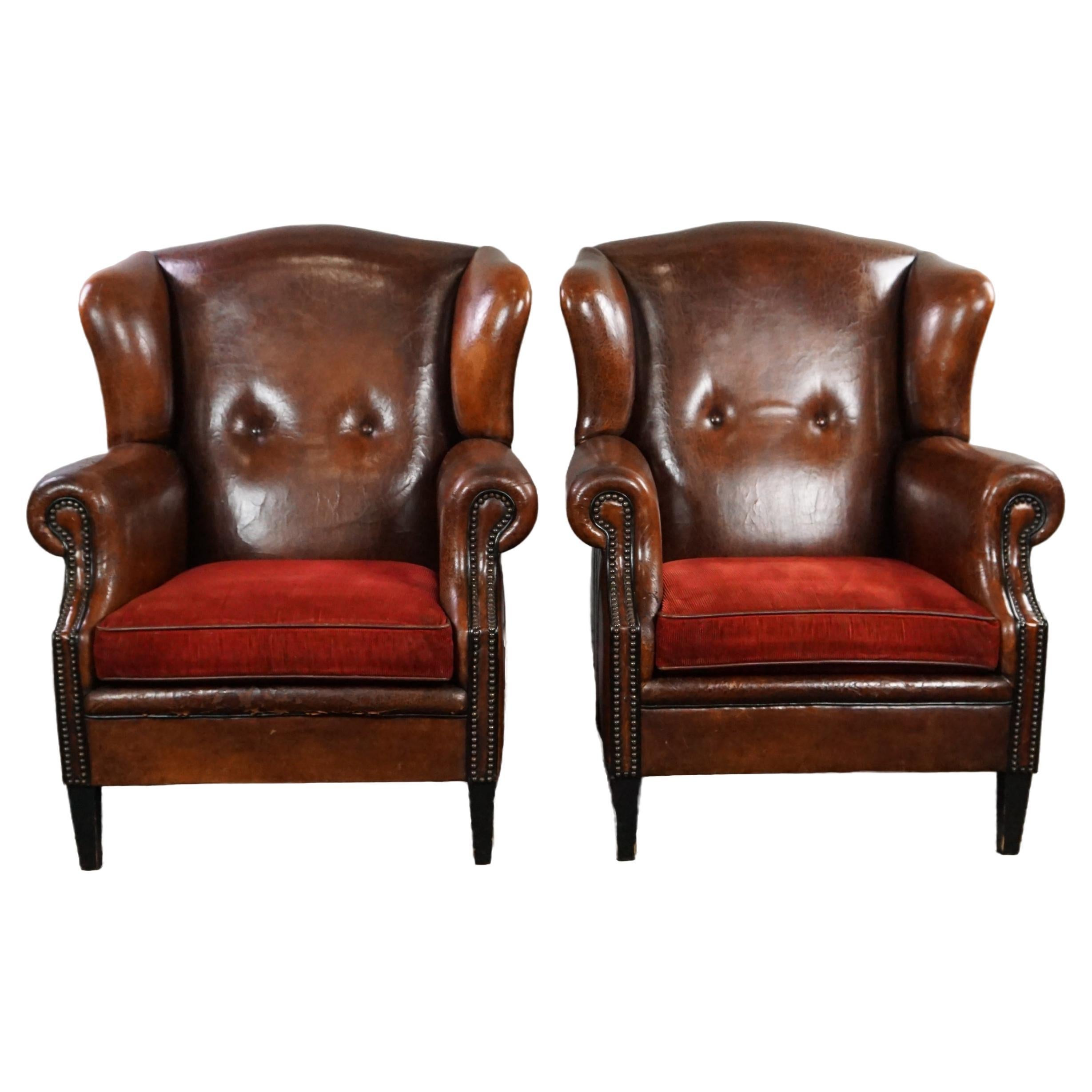 Set of two stylish sheep leather wing chairs with red corduroy seat cushions For Sale