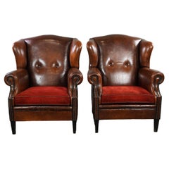 Set of two stylish sheep leather wing chairs with red corduroy seat cushions