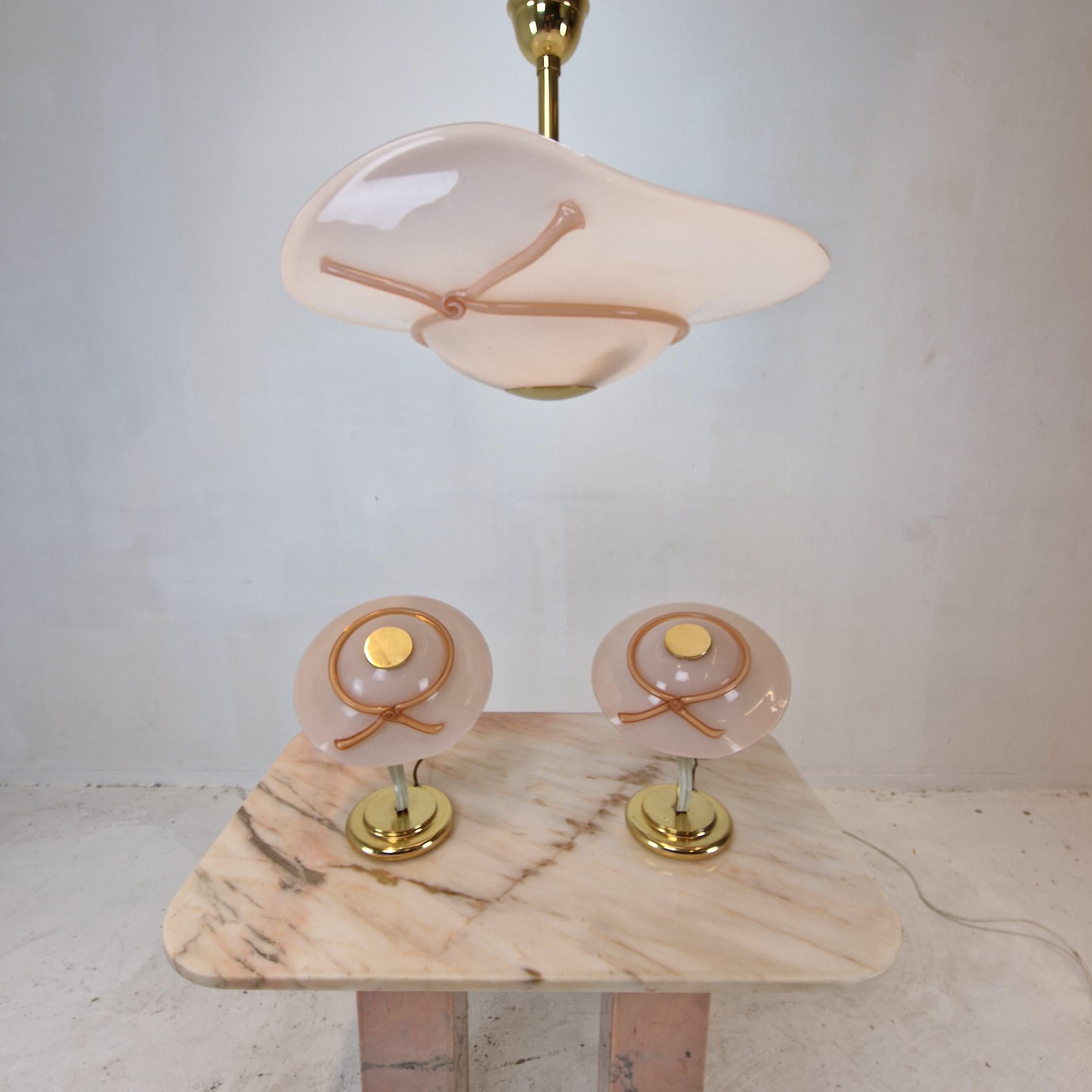 Very beautiful set of two table lamps and one pendant.
This exceptional set is fabricated in the 70's in Italy.

The hand blown glass shades are made in Murano.
All 3 shades have the same shape of a lady's hat.
They are made of very nice pink Murano