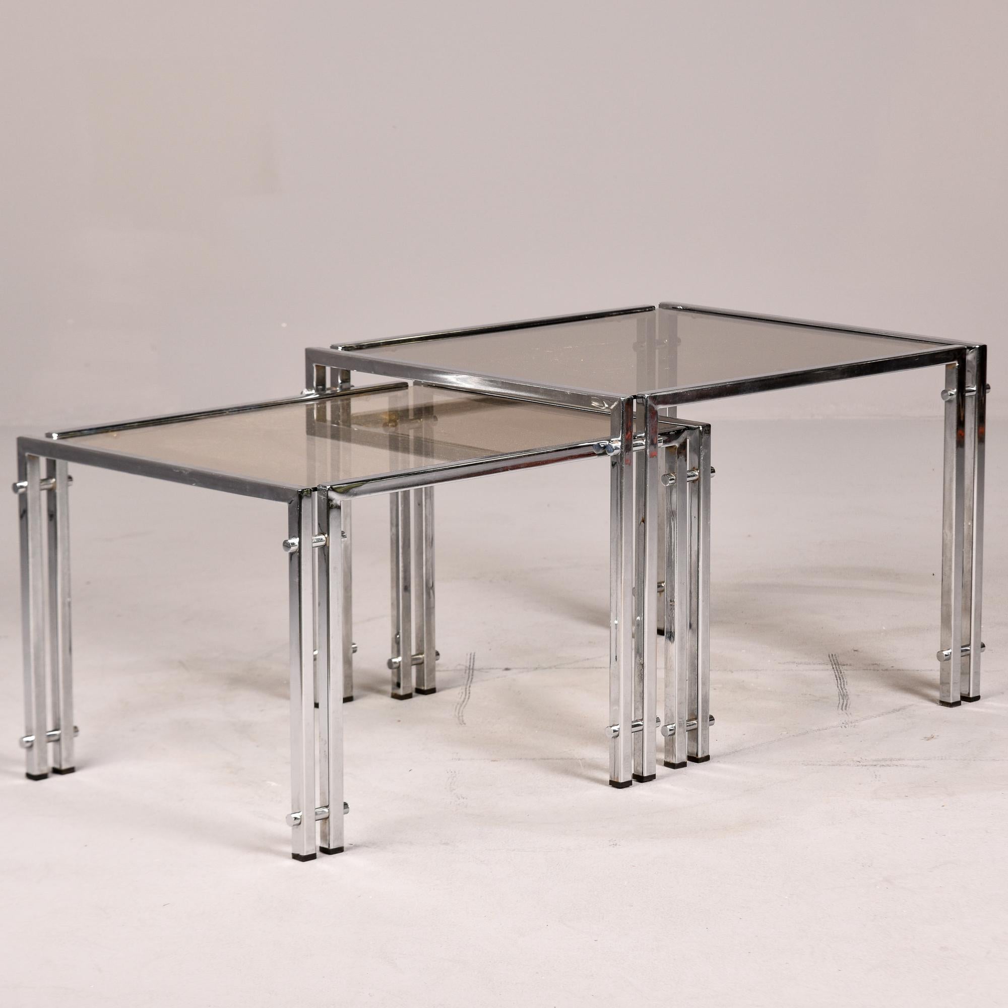 Found in Italy, this pair of circa 1970s nesting tables feature chrome frames and pale smoke-colored glass table tops. Tables have a unique double leg design. Unknown maker. Sold and priced as a set of two. Very good overall vintage condition with