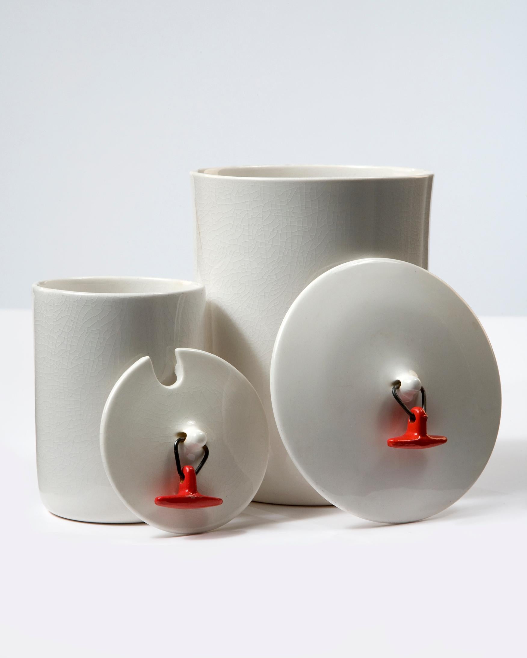 Set of two white ceramic canisters with red toggle-handled lids. Designed by La Gardo Tackett for Schmid International, Japan, 1950s.