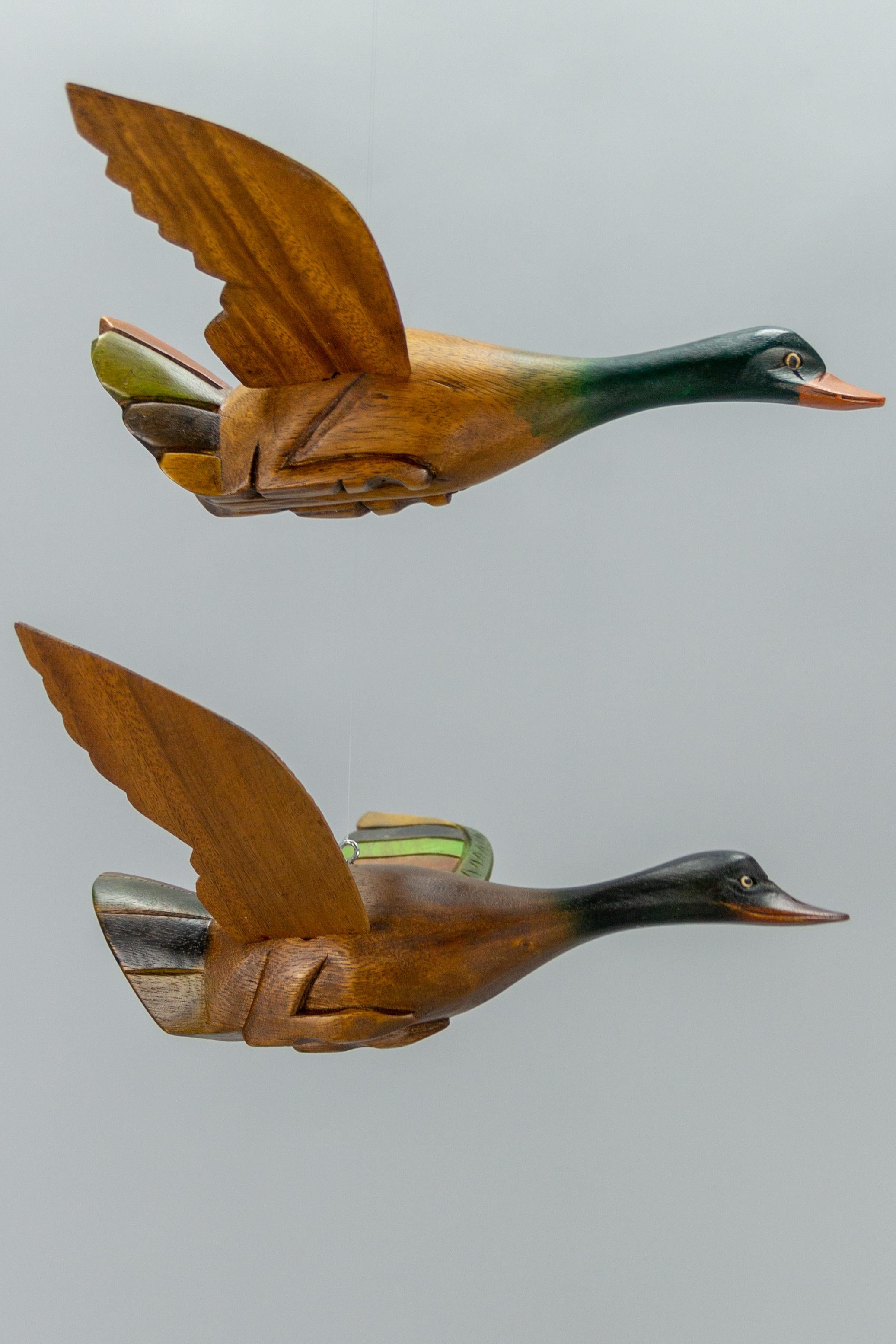 A set of two adorable carved walnut duck figures in flight painted in green, brown, and orange. The figurines are not identical, but very similar. The wings are removable. These beautiful bird sculptures can be hung and used as a nice decorative