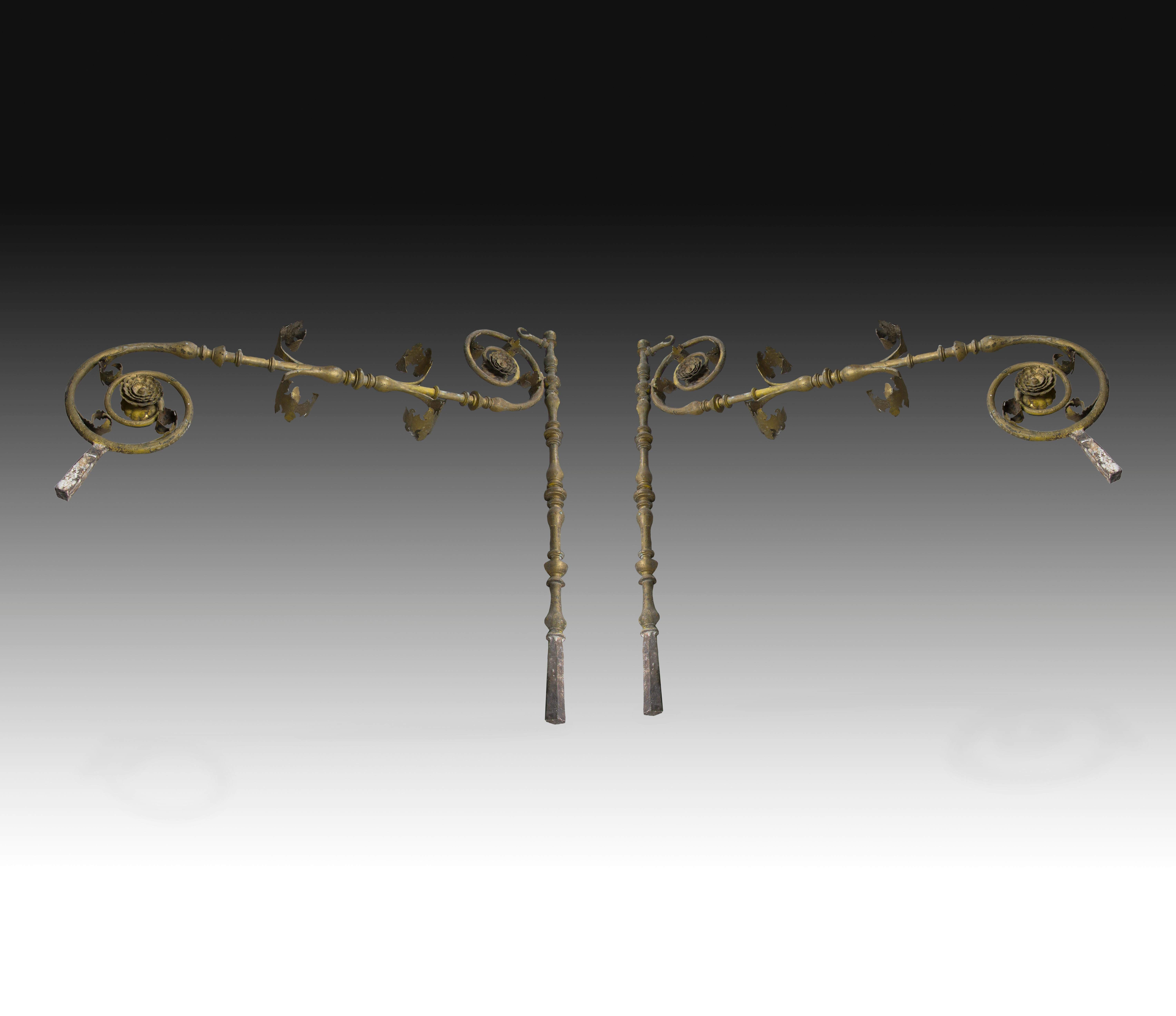 Pair of iron supports with a baluster shaped shaft, with curves and moldings reminiscent of Baroque works, and leaves, flowers and curves more related to Neoclassicism or Classical influences, with two bif flowers that might show some influence from