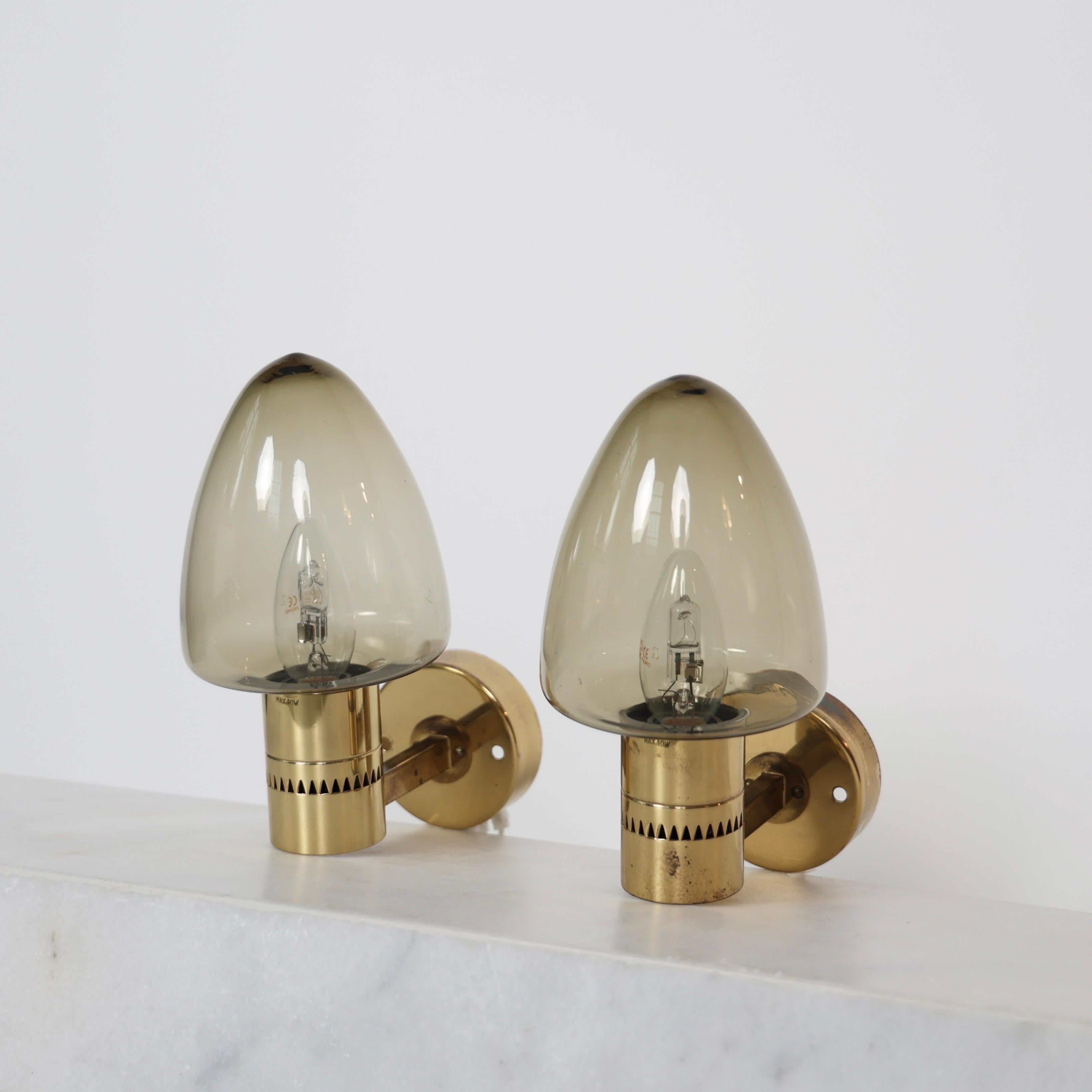 Set of Brass Sconces with Smokey Glass shades made by Hans-Agne Jakobsson in the 1960s. 

* Set (2) of brass sconces with smokey glass shades
* Designer: Hans-Agne Jakobsson
* Model: V220
* Producer: Hans Agne Jakobsson AB
* Year: 1960s
* Condition: