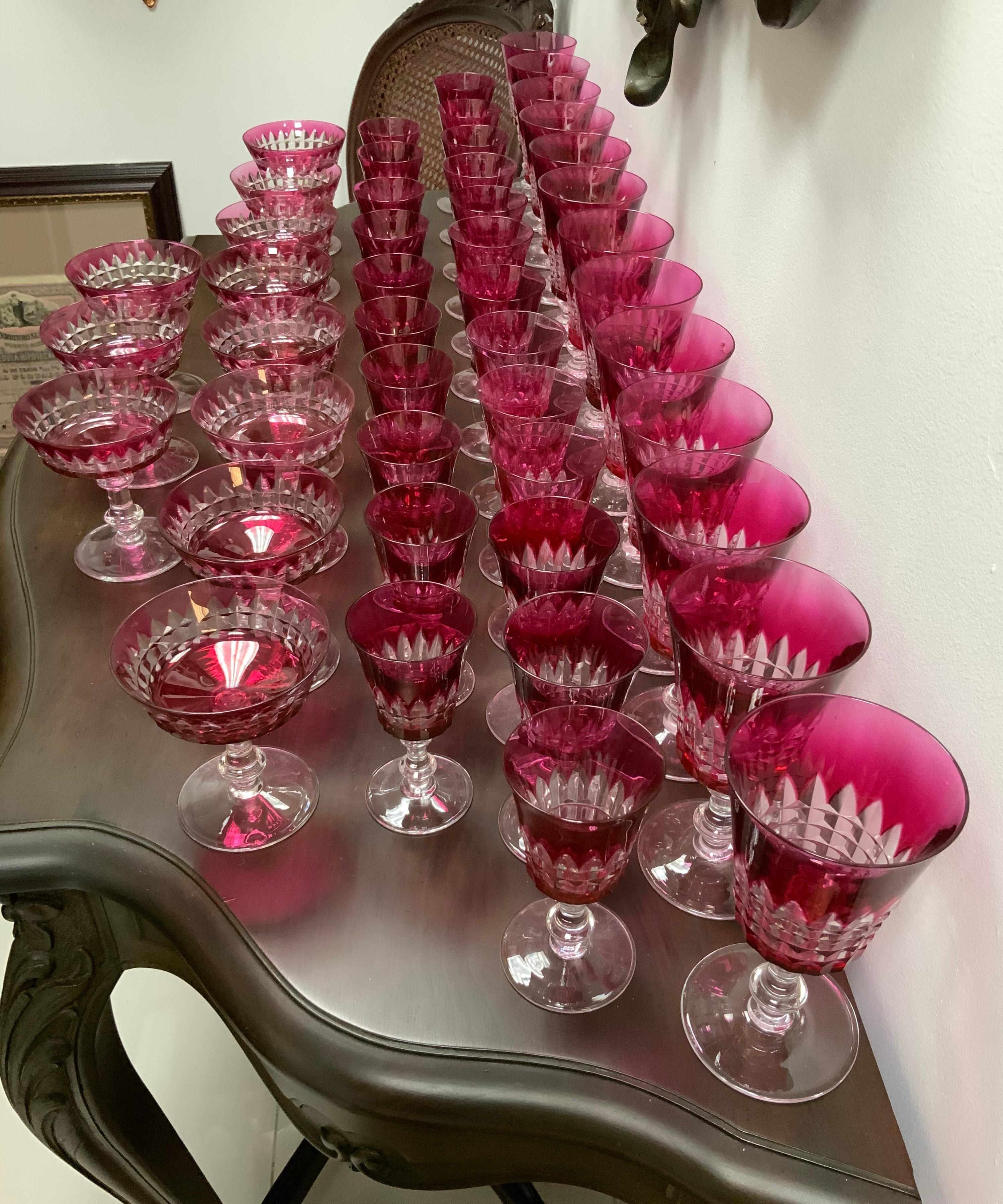 This is a set of forty five Val Saint Lambert Esneux pattern cranberry cut to clear crystal glassware. All of them are bell shaped, except one group that is circular. The bowl of the glasses are adorned with feathers pointing up and a pattern of