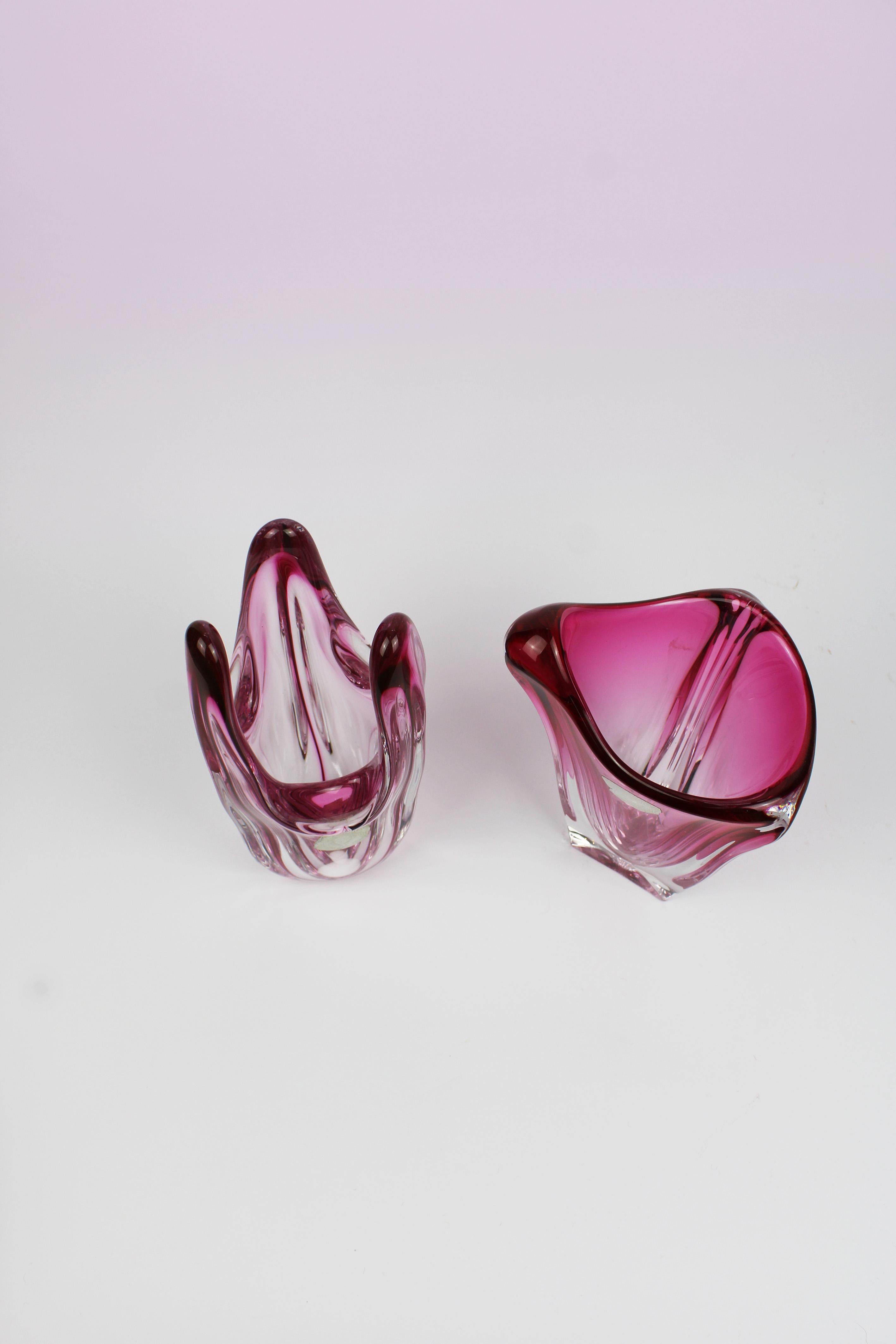 This set of vases by Val St. Lambert, the renowned Belgian glass manufacturer, truly lives up to its esteemed reputation. The distinctive design features a striking pair of vases with unique, curved shapes and a relief that transitions between pink
