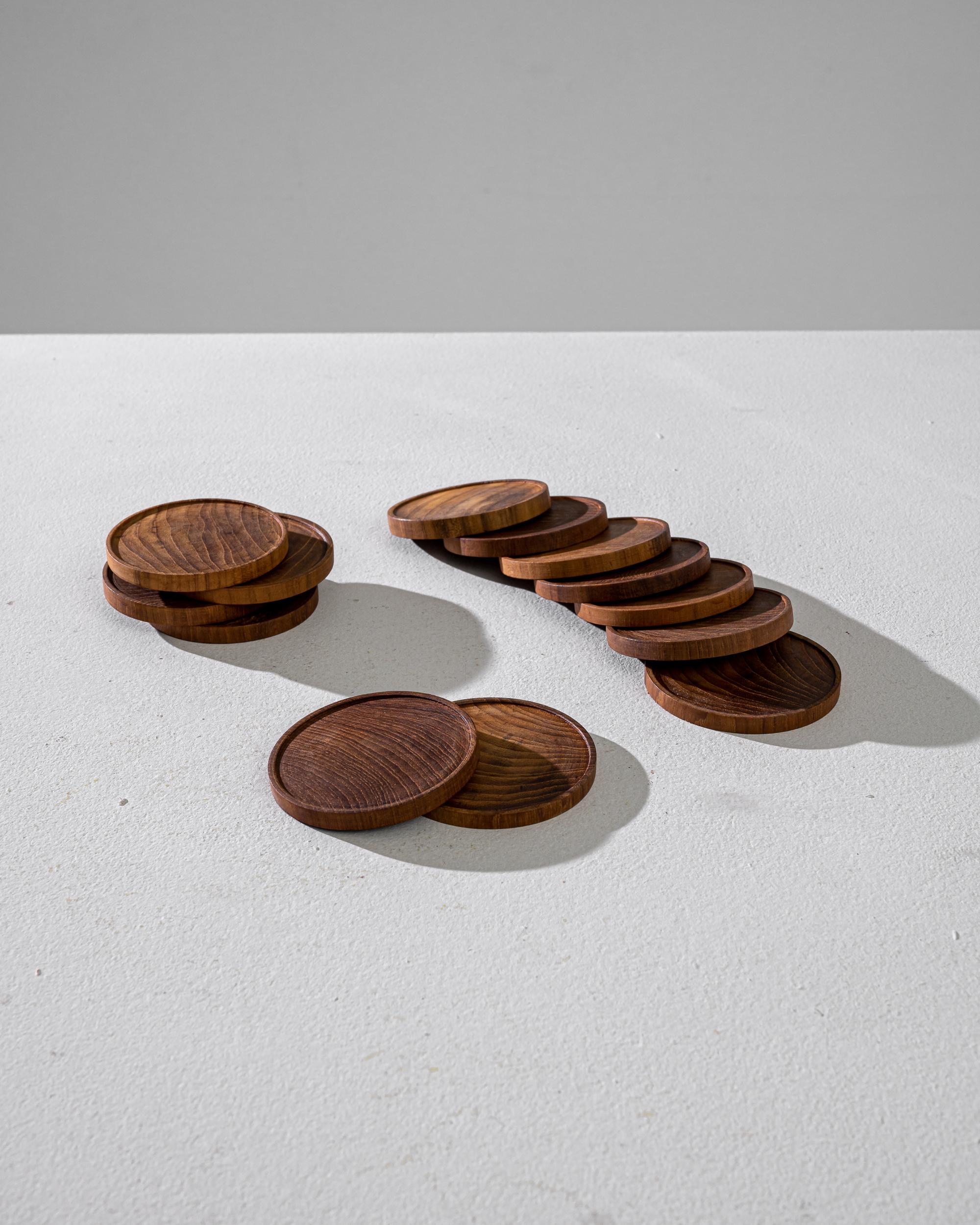 This elegant vintage set features 13 round teak coasters made in Denmark in the twentieth century. Resembling ancient wooden coins, the coasters have carved edges that prevent the drink from sliding around. The rich teak wood reveals the unique