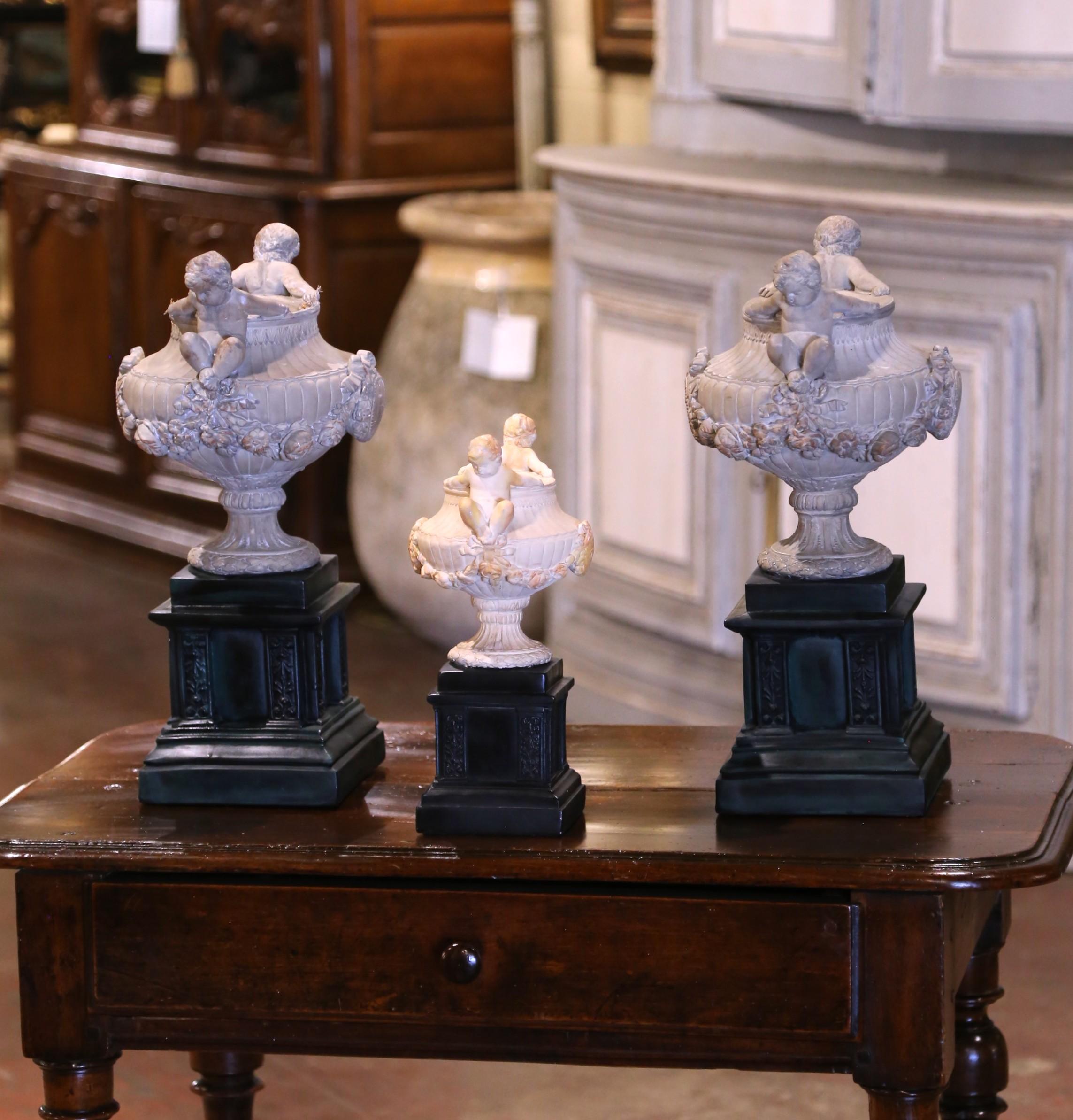 Cet élégant ensemble d'urnes vintage permet d'embellir une console ou une entrée. Fabriqué en France vers 1990, chaque pot de fleurs est conçu dans la tradition néoclassique et repose sur un haut piédestal peint en noir avec des panneaux encastrés